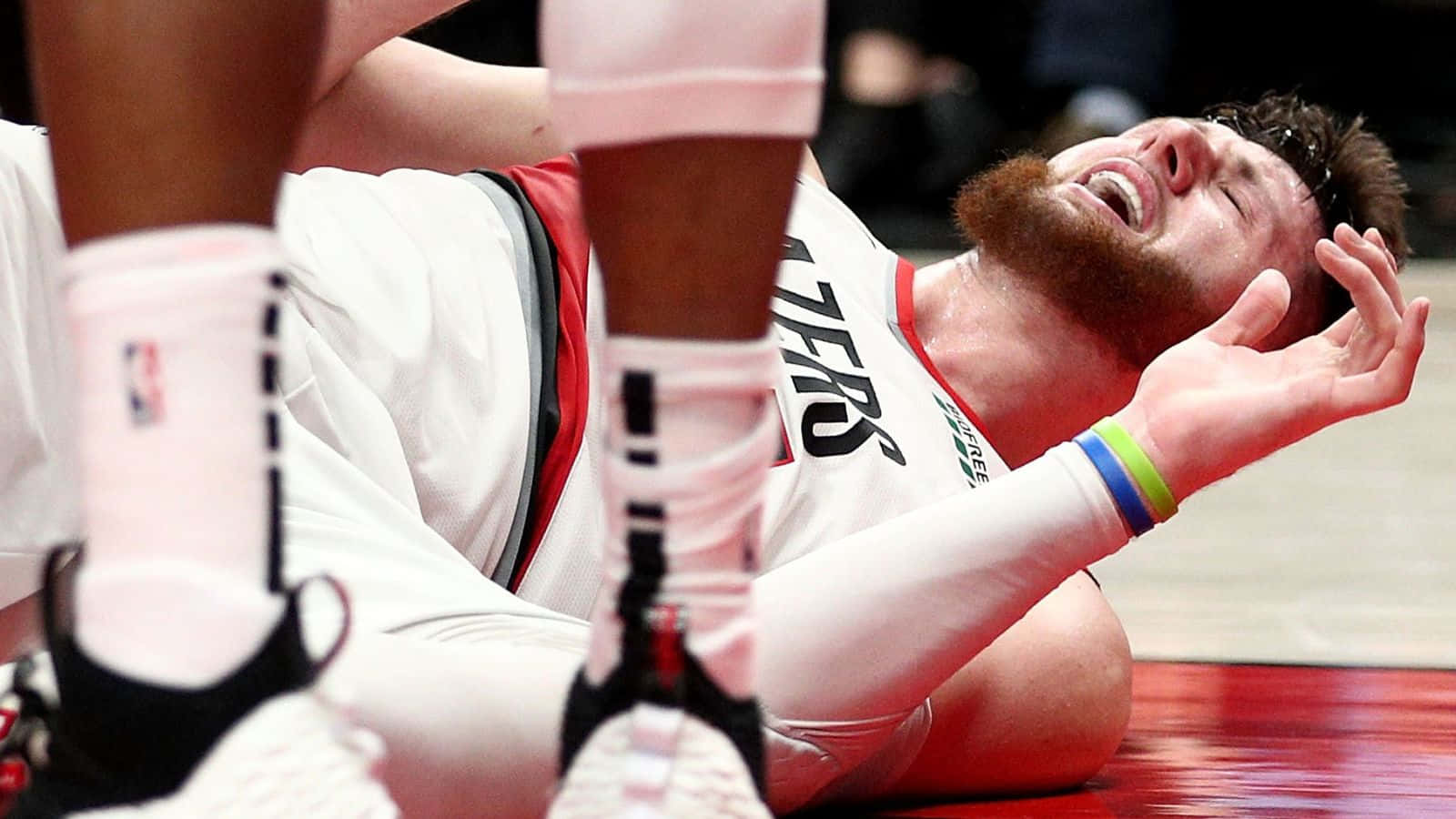 Jusuf Nurkic 對戰布魯克林籃網隊腿部受傷 壁紙 — 一名身穿白色球衣的籃球運動員在比賽中躺在紅色球場上，痛苦地抱著頭。