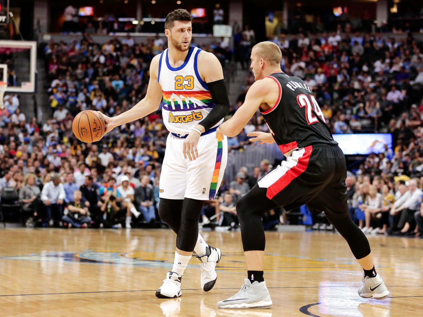 Jusuf Nurkic 與 Drew Eubanks 壁紙 — 一位身穿彩虹主題球衣的籃球運動員在擠滿觀眾的場館比賽中運球，同時被一位身穿黑色制服的對手防守。