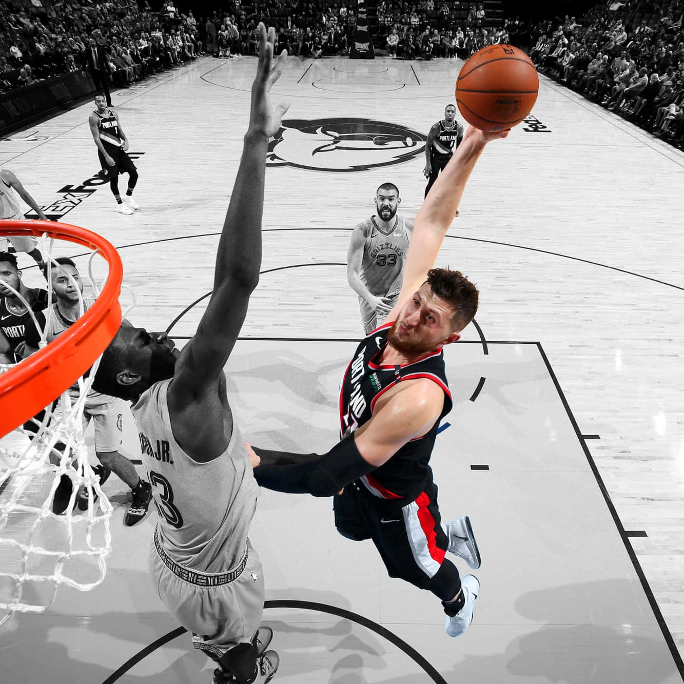 Jusuf Nurkic 與 Jaren Jackson Jr. 擊掌 壁紙 — 一名籃球運動員跳向籃框，而防守球員跳起試圖封阻他的投籃，這是一張戲劇性的黑白照片，籃框和球上帶有選擇性的橙色。