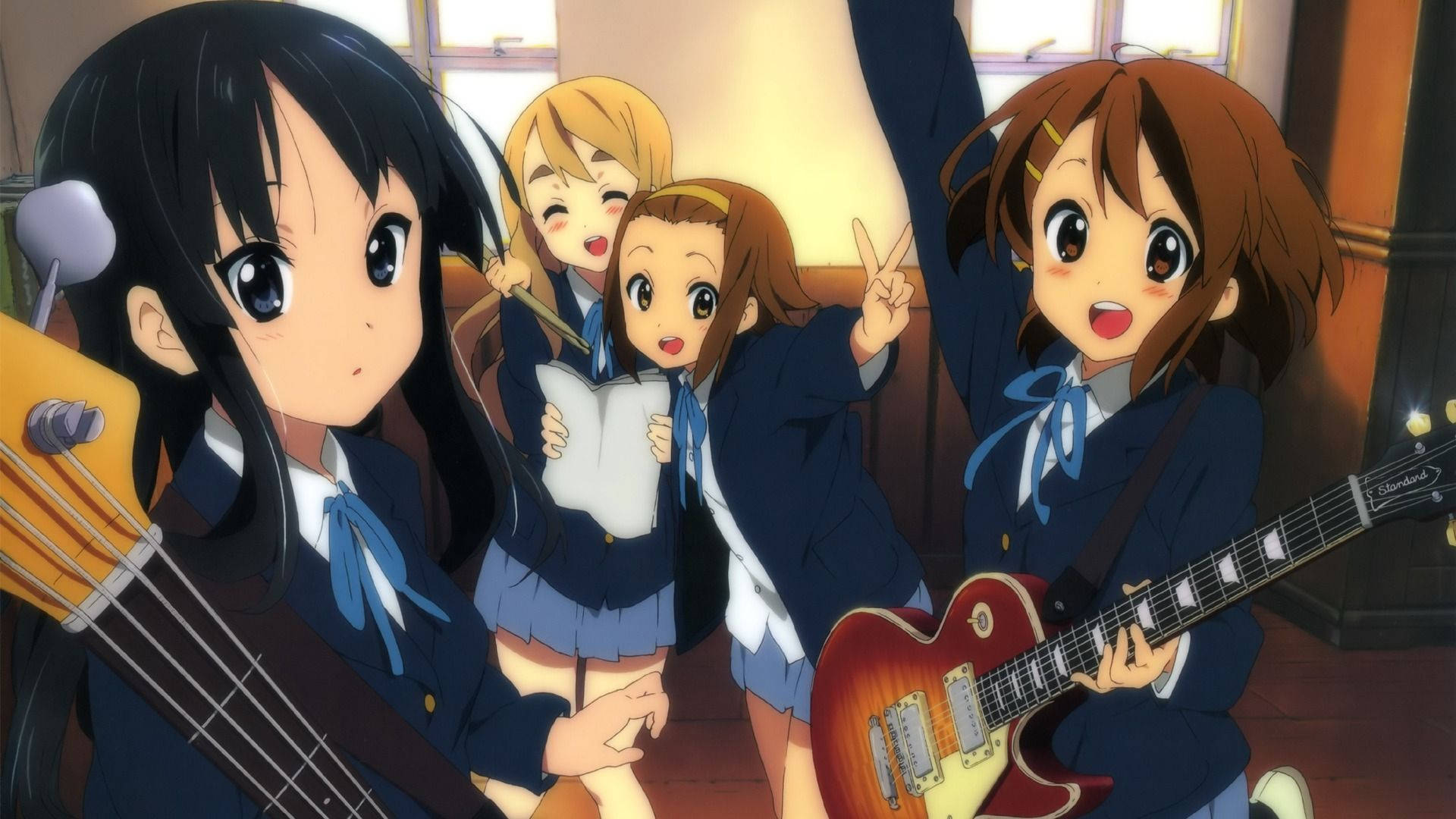 K-on 帶練習場景 壁紙 — 四個穿著校服的動漫女孩在溫暖的房間裡彈結他，並以燦爛的表情歡呼。