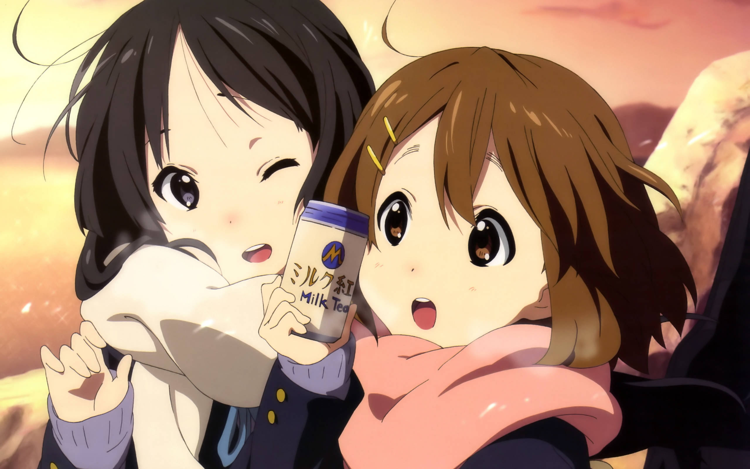 K-on Yui與Mio 壁紙 — 兩個動漫女孩擁抱，其中一個拿著一杯奶茶，背景是溫暖的日落。