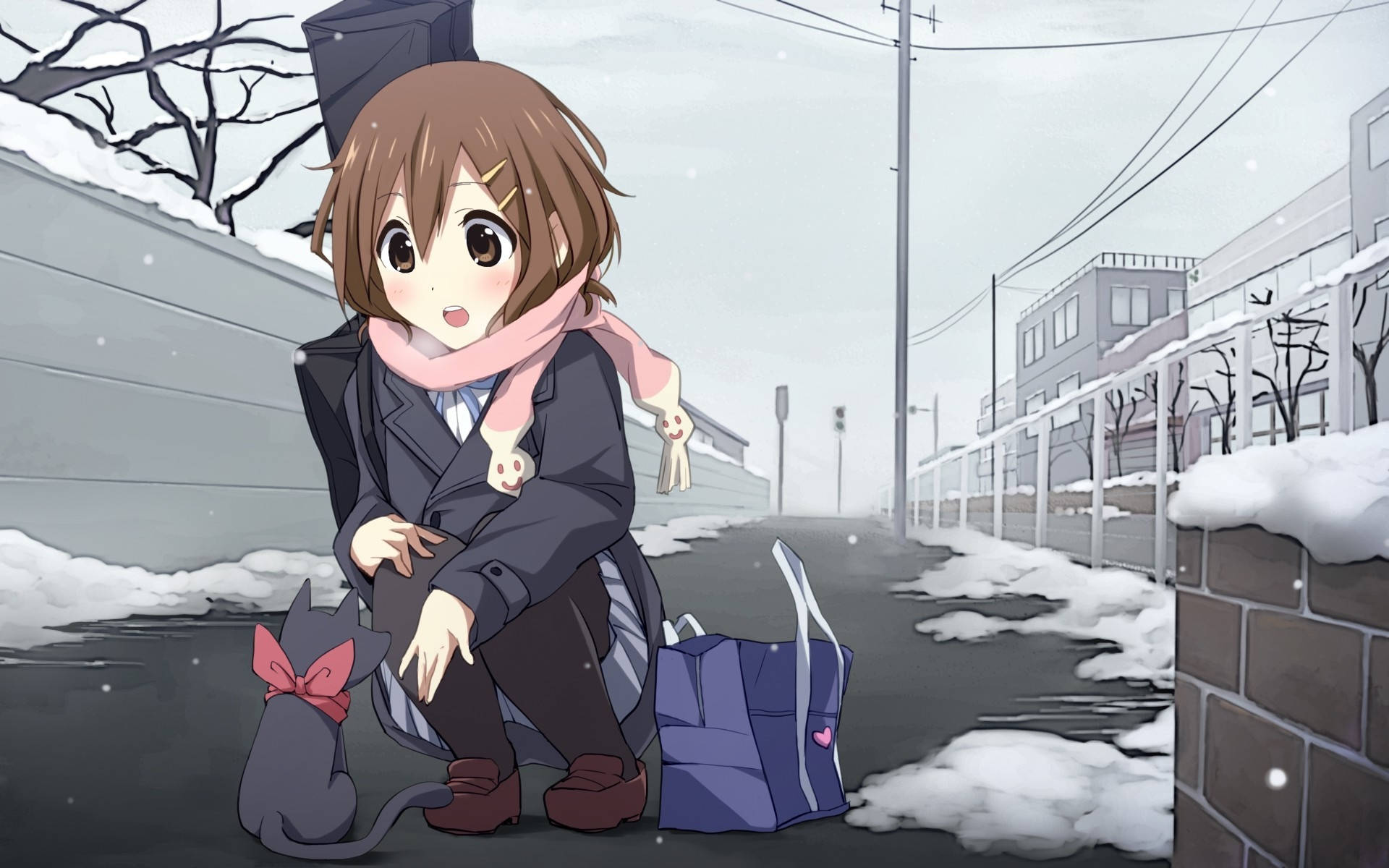 K-on 唯在路邊撫摸黑貓 壁紙 — 一個穿著冬季外套的驚訝動漫女孩蹲在一隻貓旁邊，在雪覆蓋的建築物和光禿禿的樹木的雪街上。