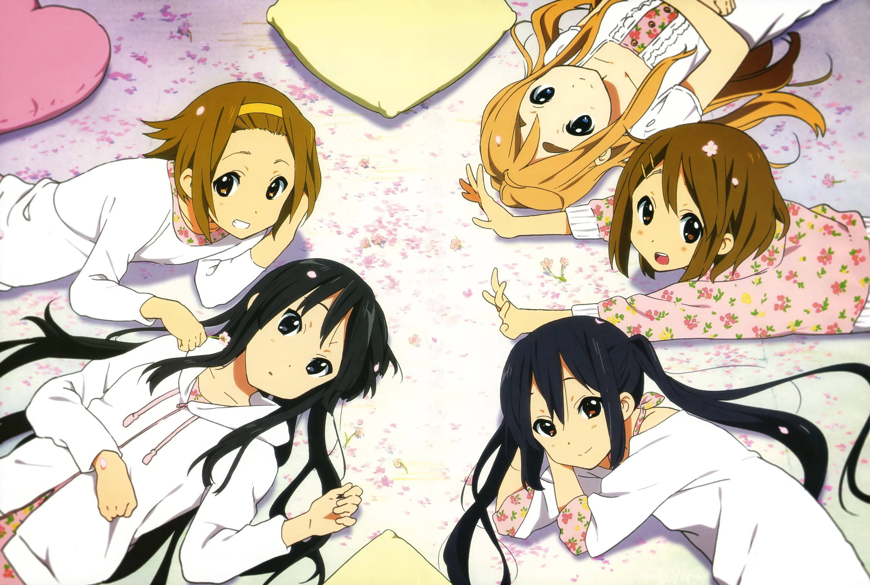 K-on 女孩睡覺聊天 壁紙 — 四個穿著睡衣的動漫女孩躺在散落著粉紅色櫻花的地板上，微笑著擺出俏皮的姿勢。
