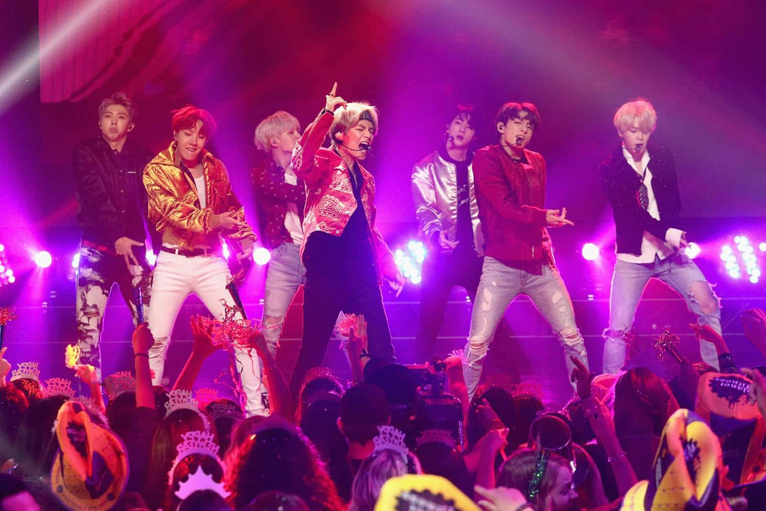 K-pop團體在舞台上表演，粉絲們戴著皇冠在下方。
