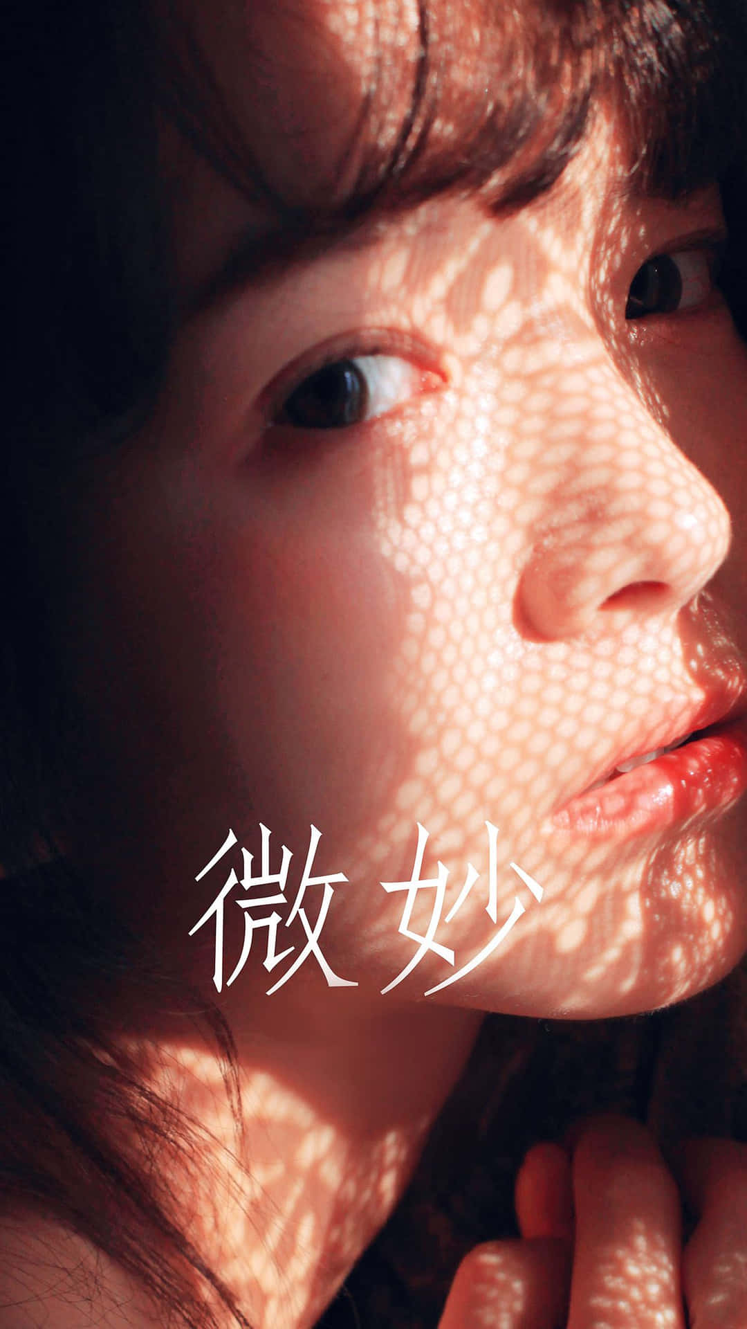 K-pop 女團舞台表演瞬間 壁紙 — 年輕女子臉部的特寫肖像，沐浴在穿過樹葉的溫暖陽光中，在肌膚上投下斑駁的陰影。
