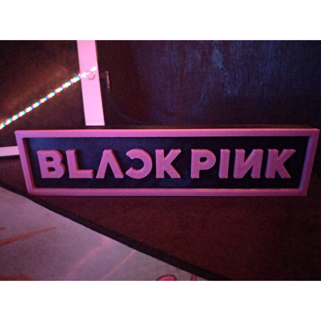 在黑暗房間中，帶有LED燈的粉紅色發光BLACK PINK標誌。