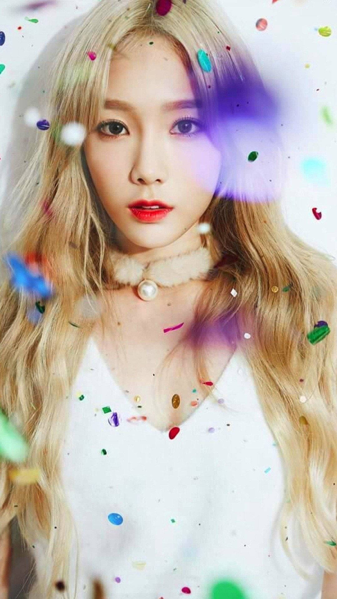 K-pop天后泰妍在絢麗紙屑中盡顯魅力 壁紙 — 一位金髮紅唇的年輕女性向前凝視，色彩繽紛的紙屑在明亮的攝影棚中圍繞她旋轉。