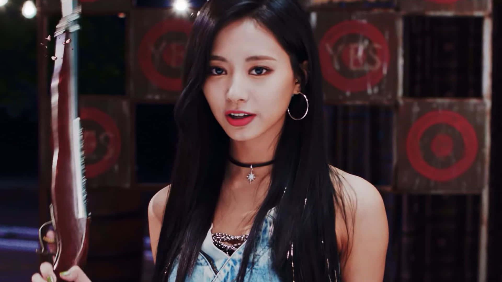 K-pop天團TWICE準備登台 壁紙 — 一位長黑髮的年輕女性，戴著頸鏈和星星吊墜，手持步槍，背景是紅色靶板。