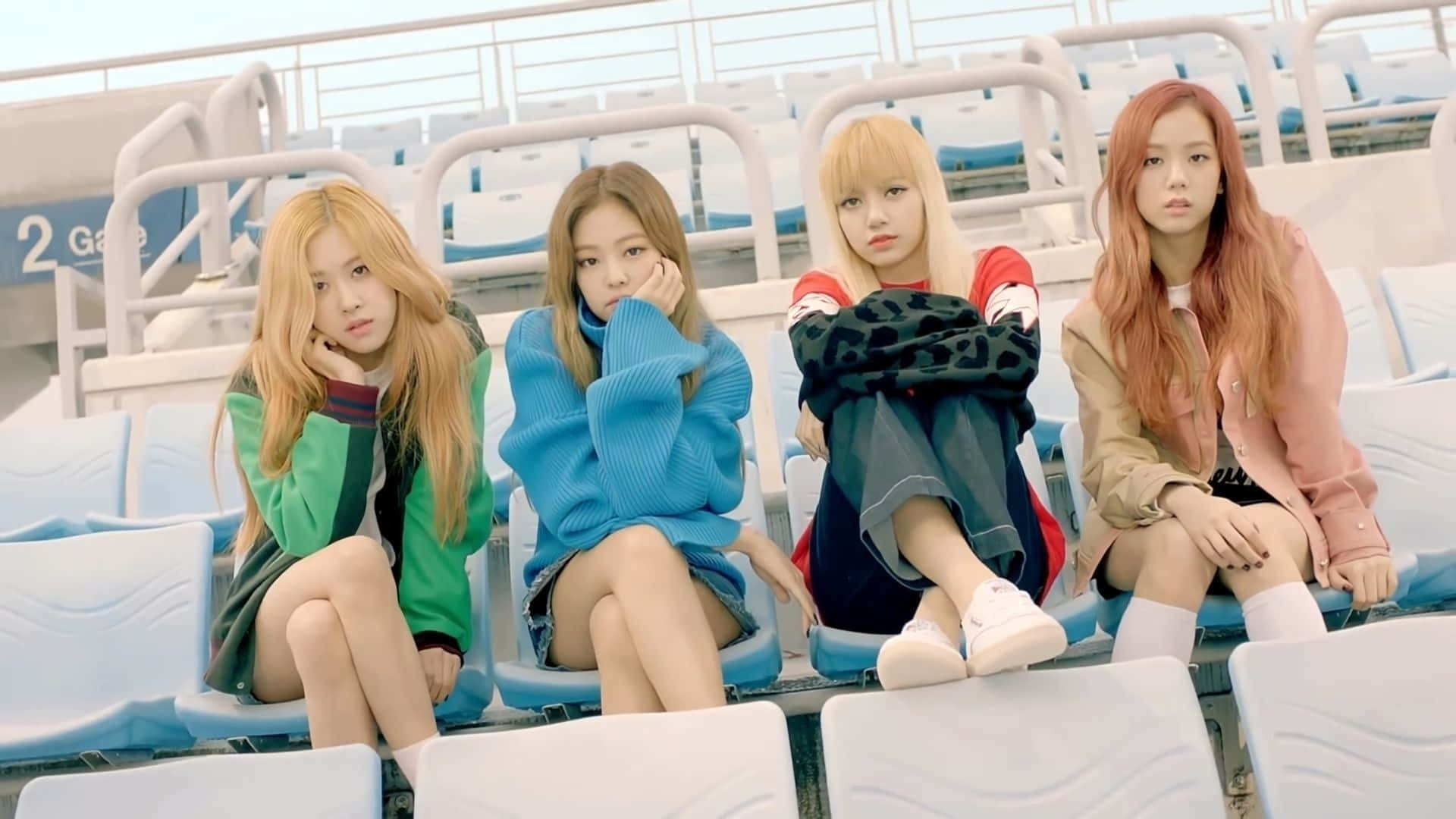 K-pop巨星引爆舞台 壁紙 — 四位時尚年輕女性坐在體育場座位上，在明亮的日光下露出沉思的表情。
