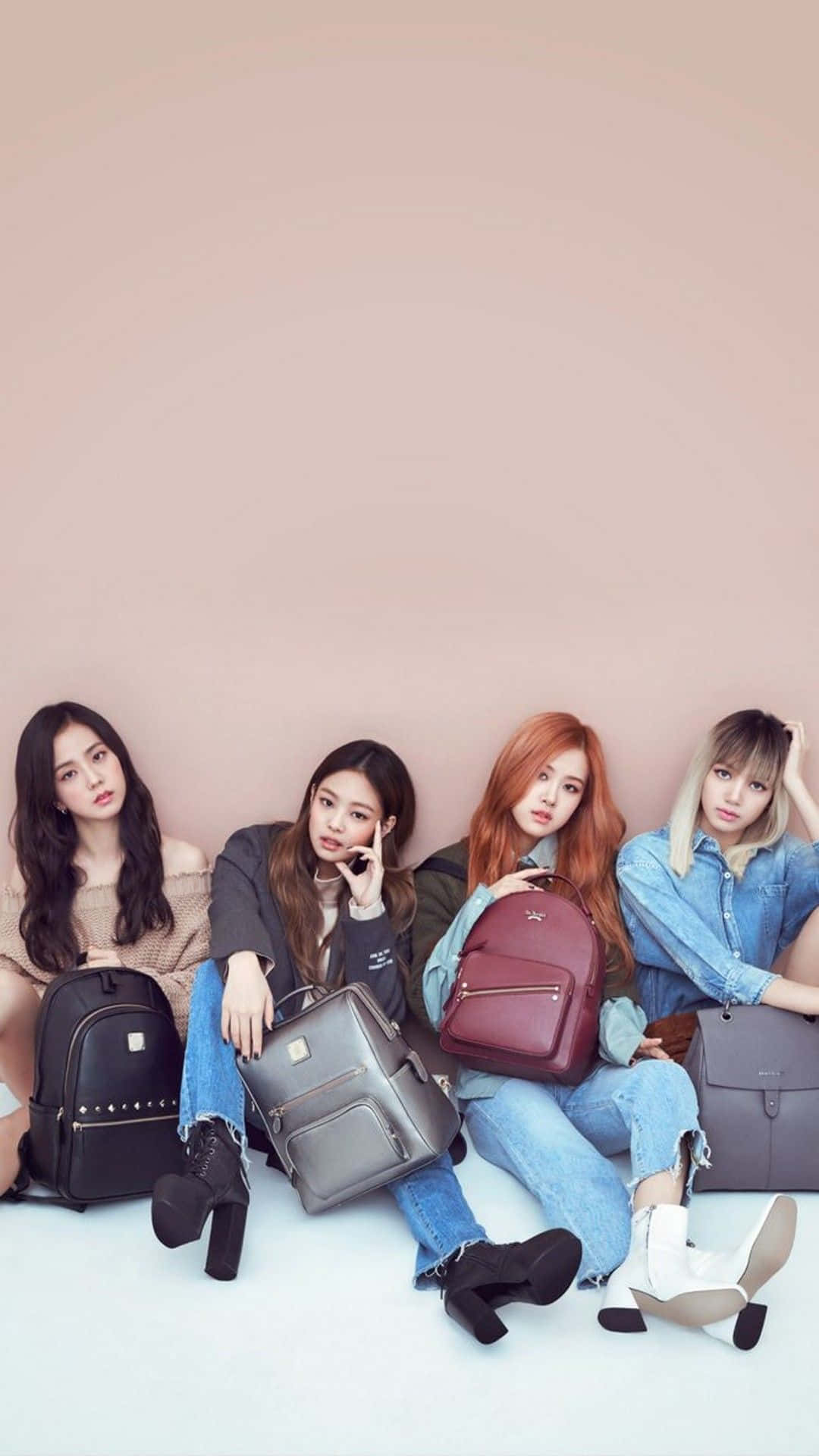 K-pop巨星舞台造型 壁紙 — 四位時尚年輕女性在白色地板上對著柔和的粉紅色牆壁隨意擺姿勢，每人手持一個設計師背包。