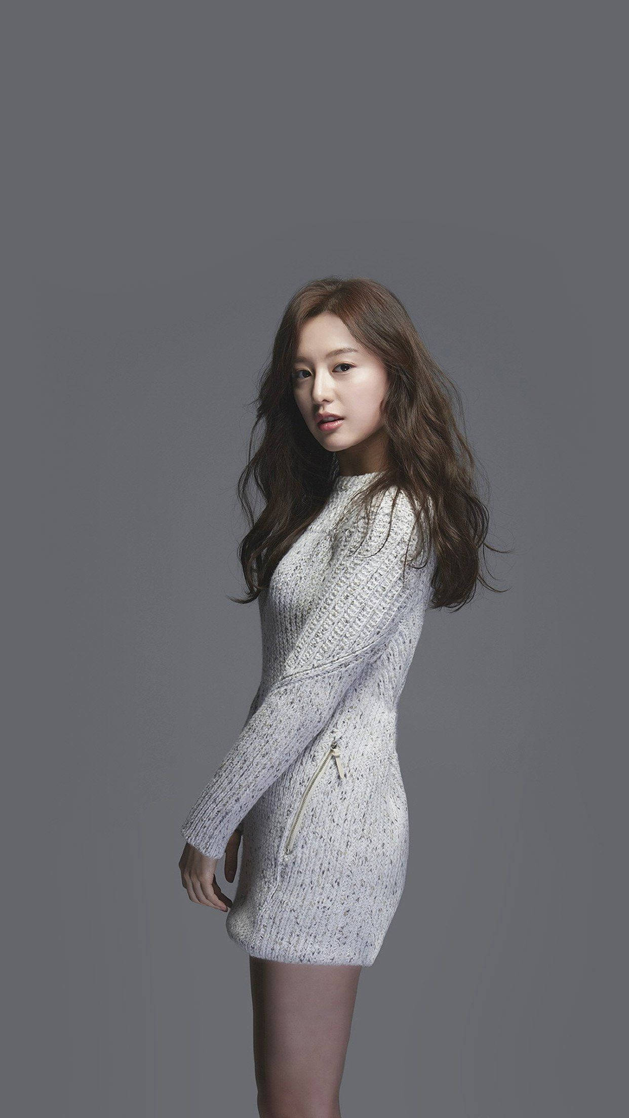 K-pop演員金智媛 壁紙 — 一位身穿質感白色針織連衣裙的女性在柔和的燈光下，在純灰色工作室背景前擺姿勢。