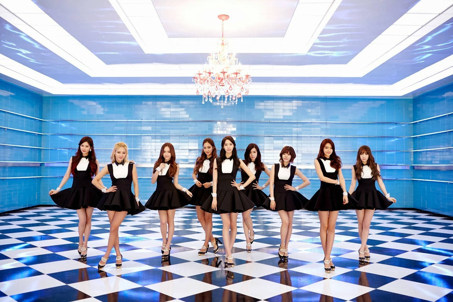 K-POP能量爆發：音樂重新定義 壁紙 — 九位身穿黑白服裝的女性，在未來感藍色房間的水晶吊燈下，自信地站在藍白格子地板上。