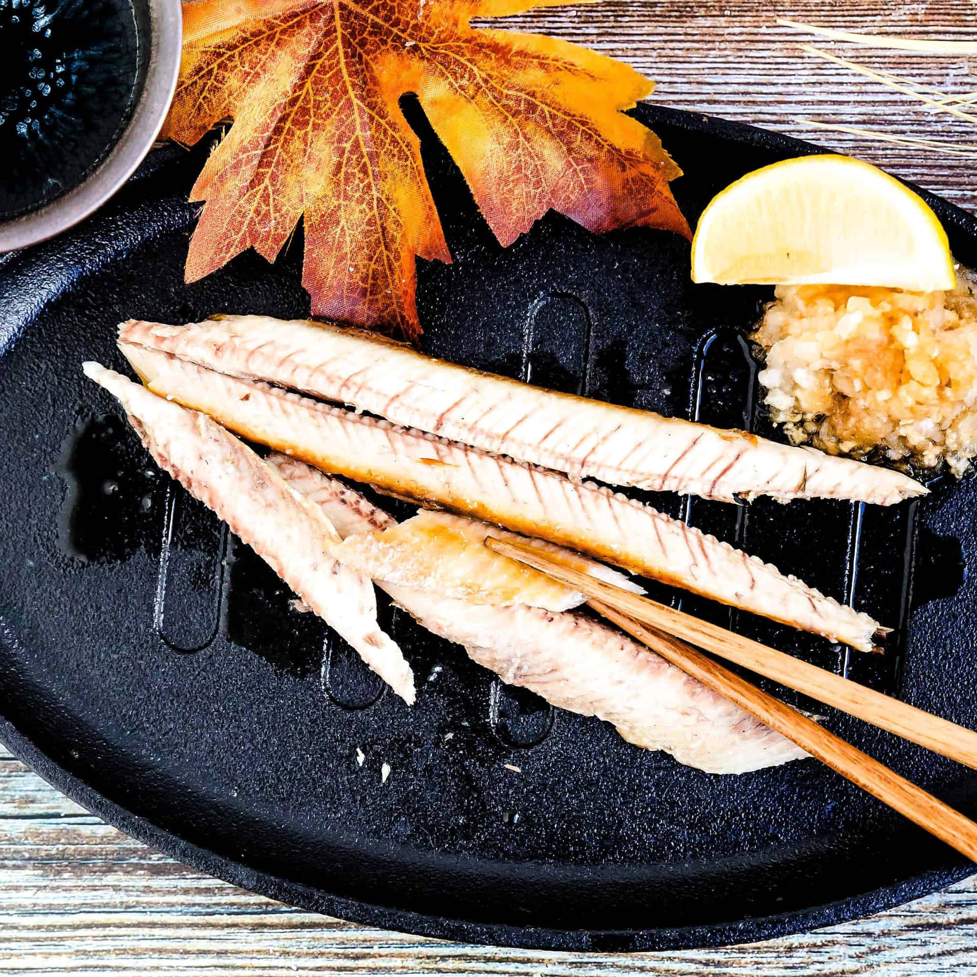  壁紙 — 烤魚柳放在黑色烤盤上，飾以秋葉、檸檬和米飯，配筷子。