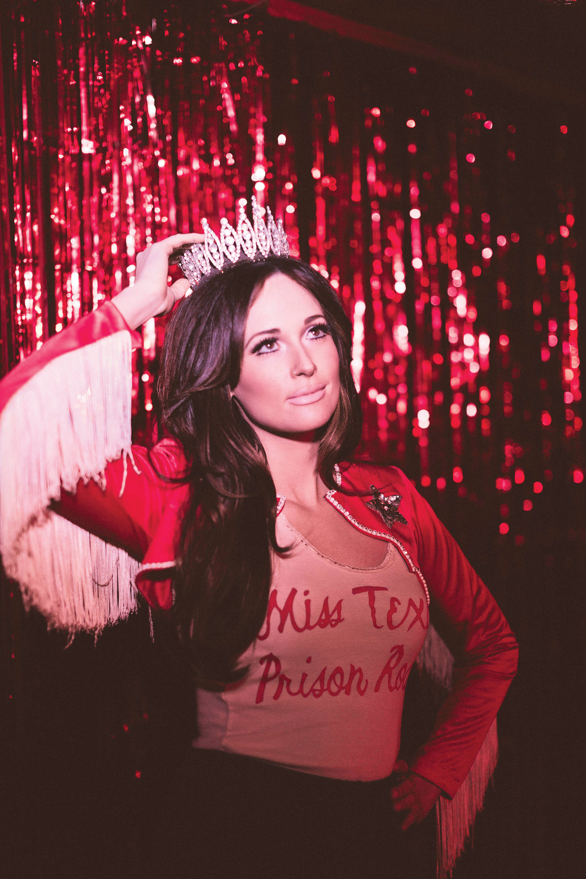 Kacey Musgraves《Pageant Material》專輯封面 壁紙 — 一位身穿紅色流蘇外套和頭戴皇冠的女性，在閃閃發光的紅色窗簾背景下自信地擺姿勢。