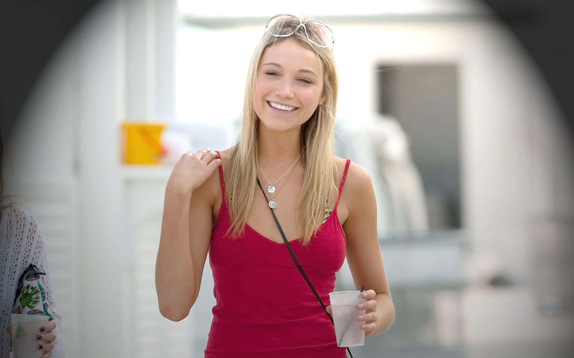 Katrina Bowden 桌布 壁紙 — 一位開朗的金髮女性穿著紅色上衣，微笑著拿著杯子，頭上戴著太陽眼鏡。