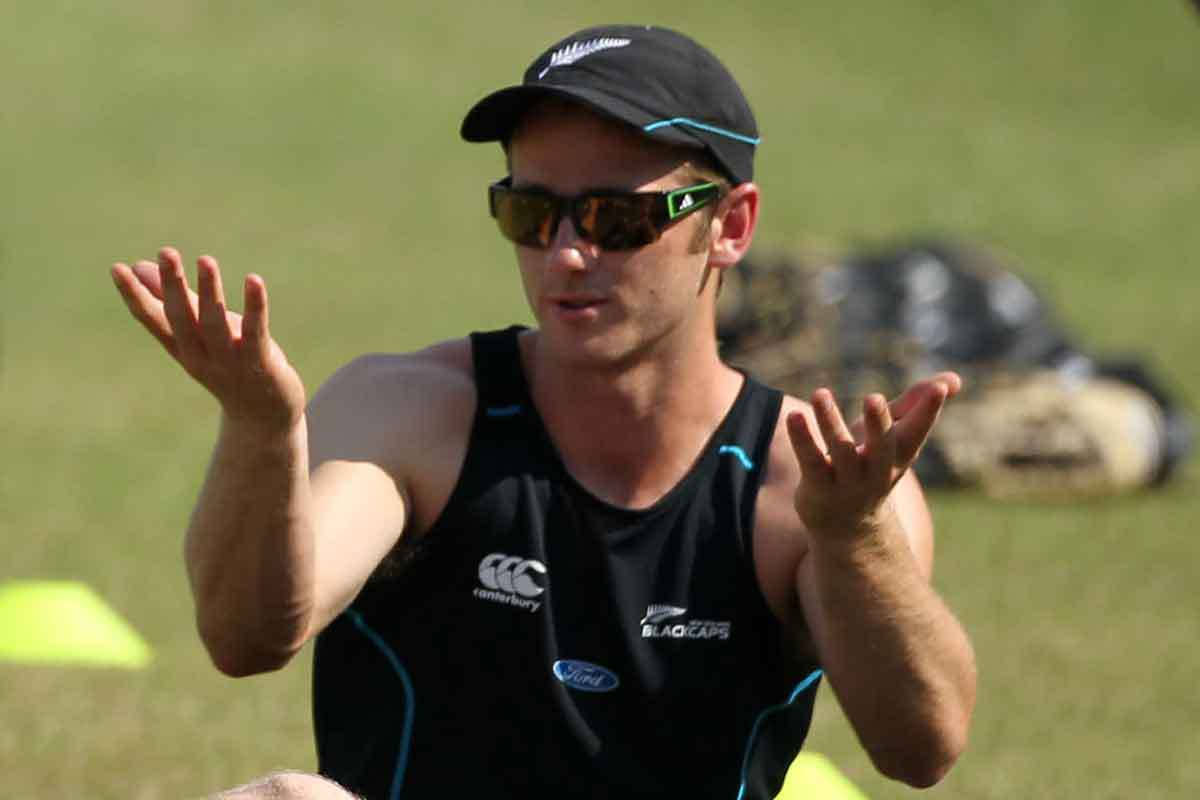 Kane Williamson 專業板球員 壁紙 — 一名新西蘭板球運動員身穿黑色訓練球衣和帽子，在陽光明媚的草地上生動地做手勢。
