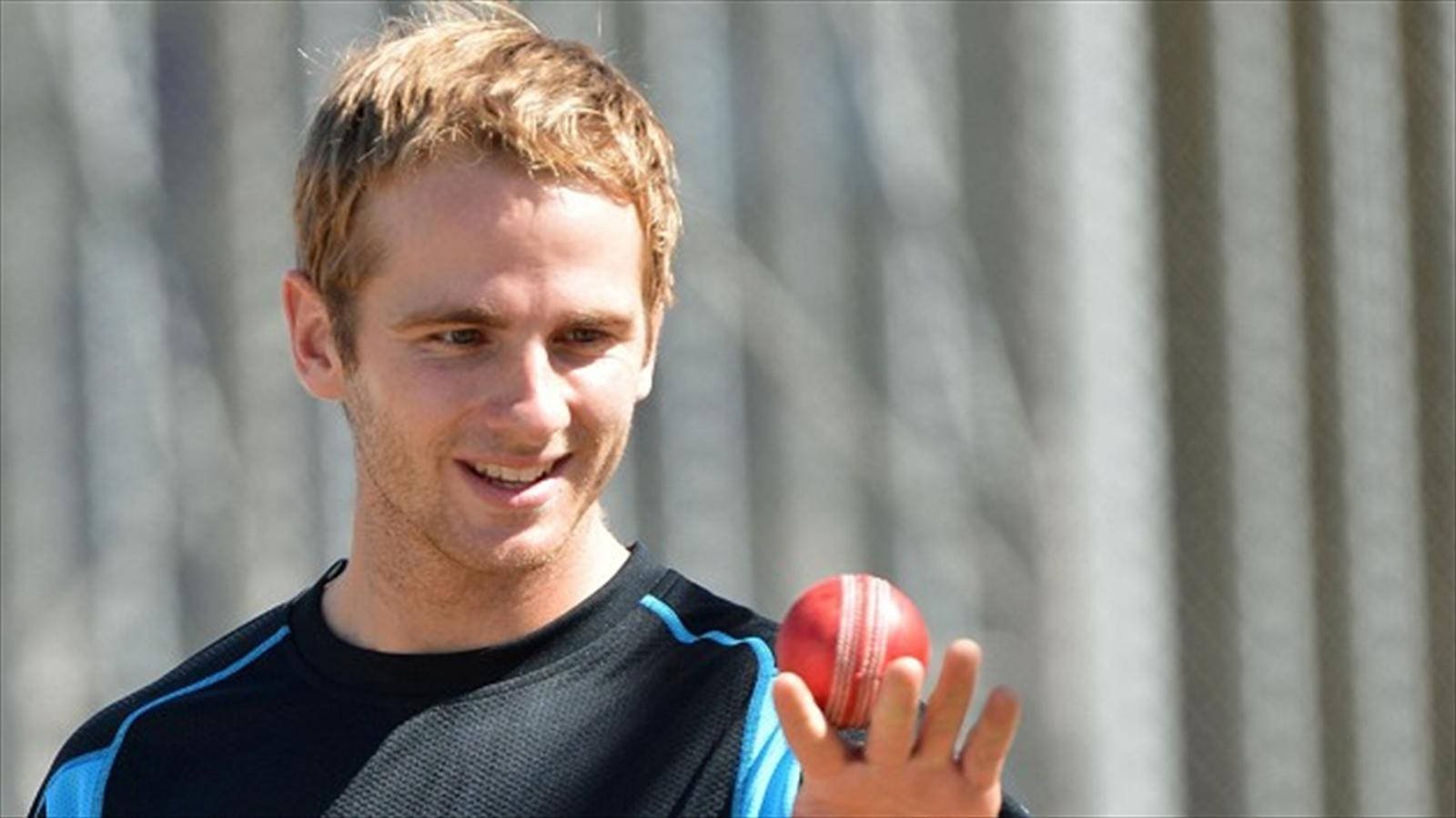 Kane Williamson 手持板球 壁紙 — 一位微笑的板球手在模糊的灰色波紋背景前手持一個紅色皮革板球。