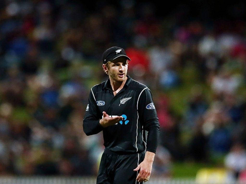 Kane Williamson 板球場上 壁紙 — 一名身穿黑色制服的新西蘭板球運動員在夜間比賽中，在球場燈光下做出手勢，背景是模糊的人群。