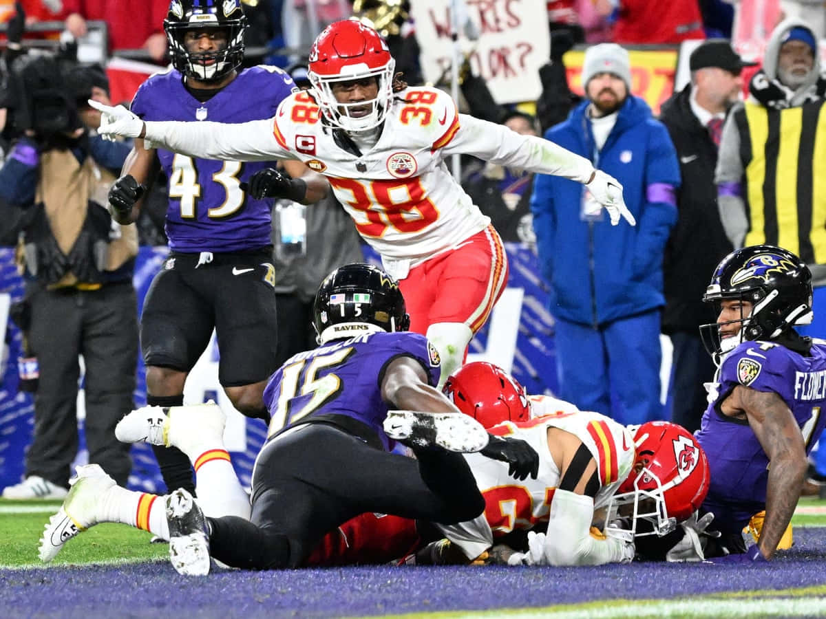  壁紙 — 一名身穿紅白色球衣的堪薩斯城酋長球員在激烈的NFL美式足球攔截中跳過一堆巴爾的摩烏鴉球員。