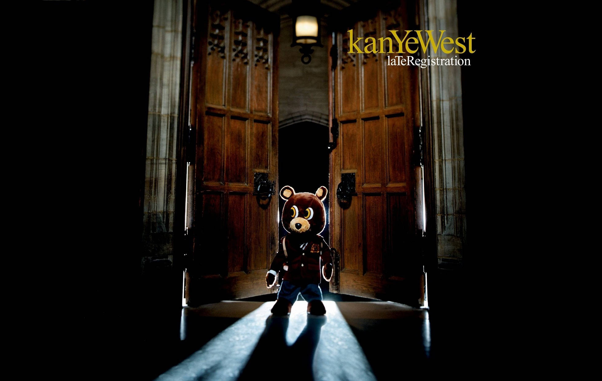 Kanye West《Late Registration》專輯封面 壁紙 — 一隻泰迪熊吉祥物站在聚光燈下，位於昏暗大廳中宏偉木門的門檻處。