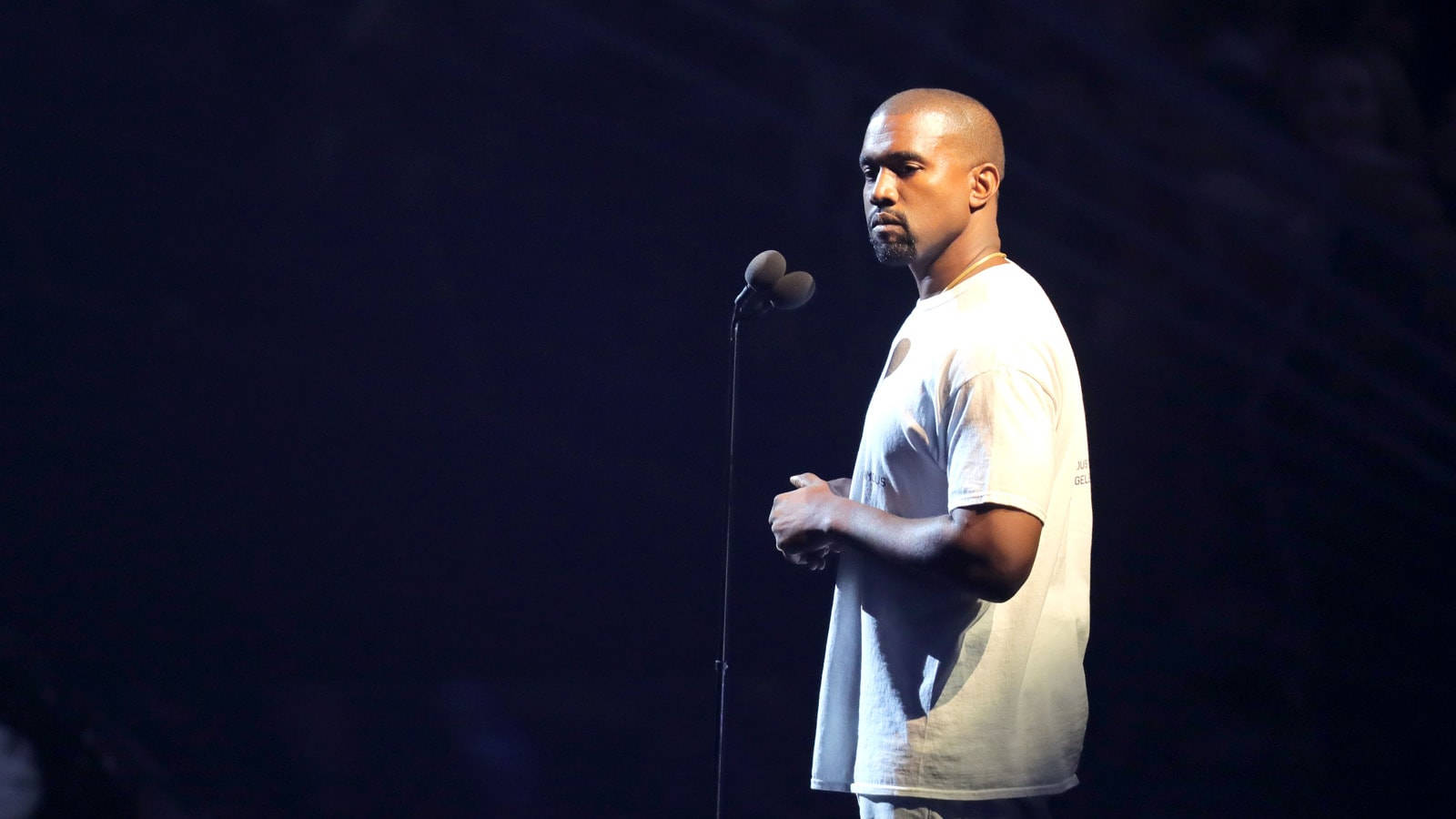 Kanye West 在黑暗舞台上於聚光燈下表演，穿著白色T恤。