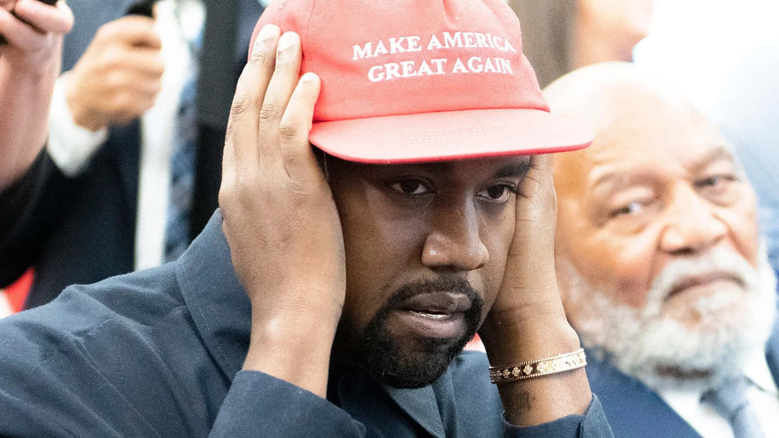 Kanye 桌布 壁紙 — Kanye West 喺公開活動戴住紅色 'Make America Great Again' 帽，同時疑似痛苦咁揞住個頭。