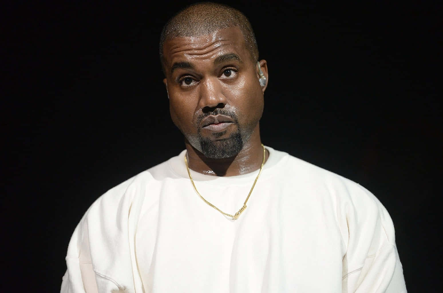 Kanye 桌布 壁紙 — Kanye West 喺黑色背景前，穿著一件純白色衛衣，戴住一條金鏈，專注地凝視。
