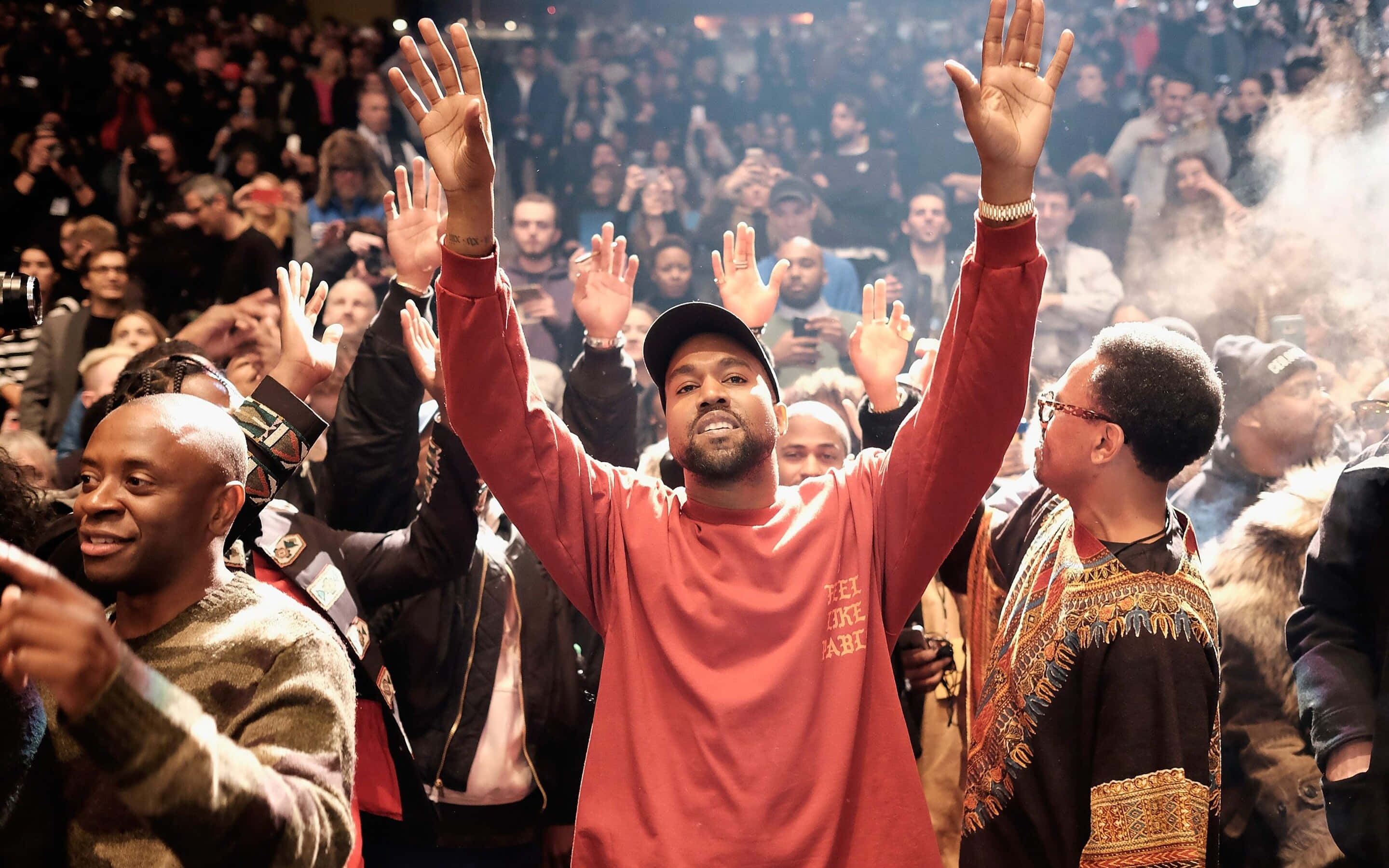 Kanye 桌布 壁紙 — Kanye West 在演唱會中於煙霧和閃光燈下在人群中舉起雙臂。