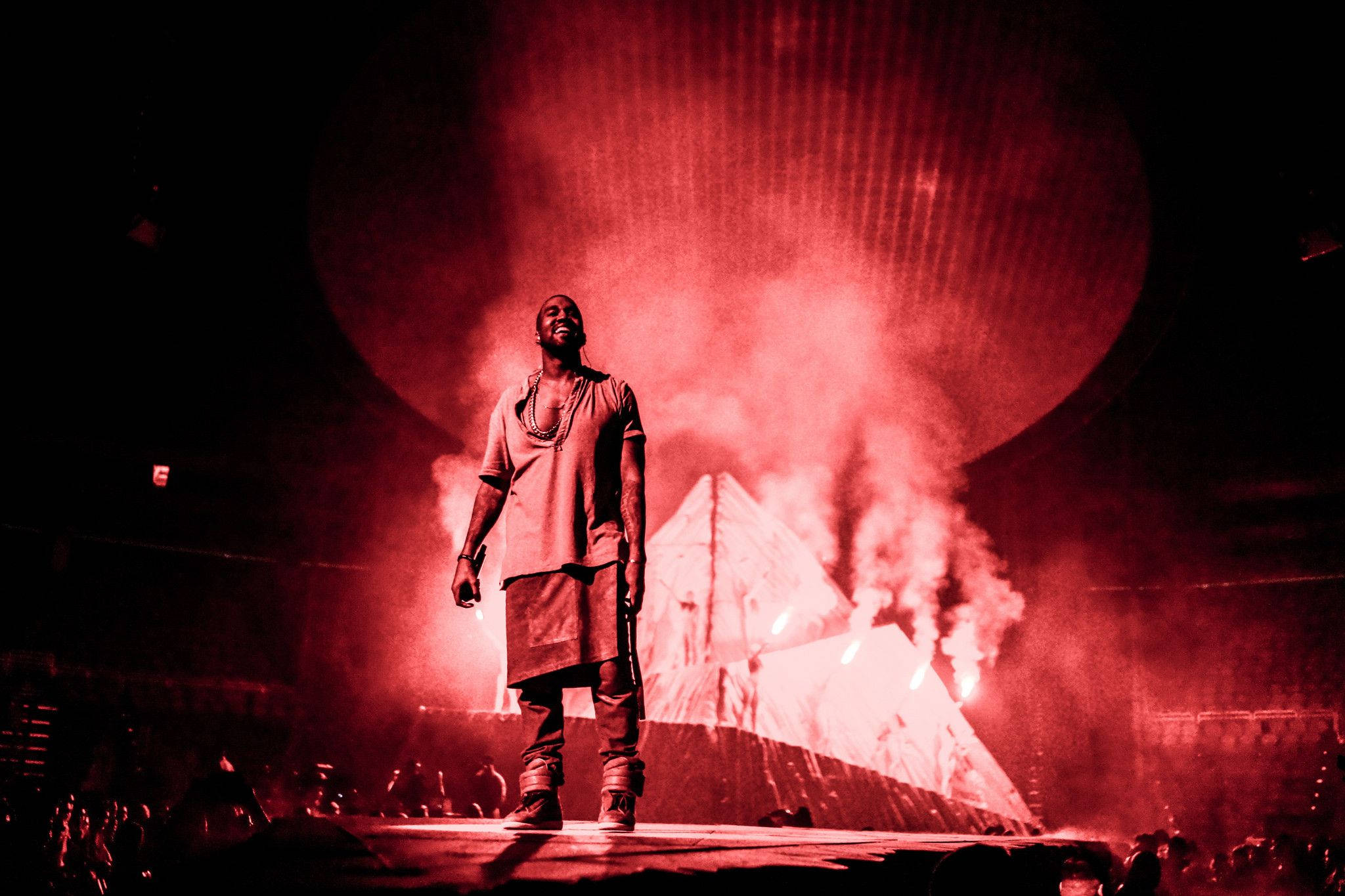 Kanye West 站在紅色舞台 壁紙 — 一位表演者站在被強烈紅光籠罩的舞台上，伴隨著煙霧和發光的金字塔背景。