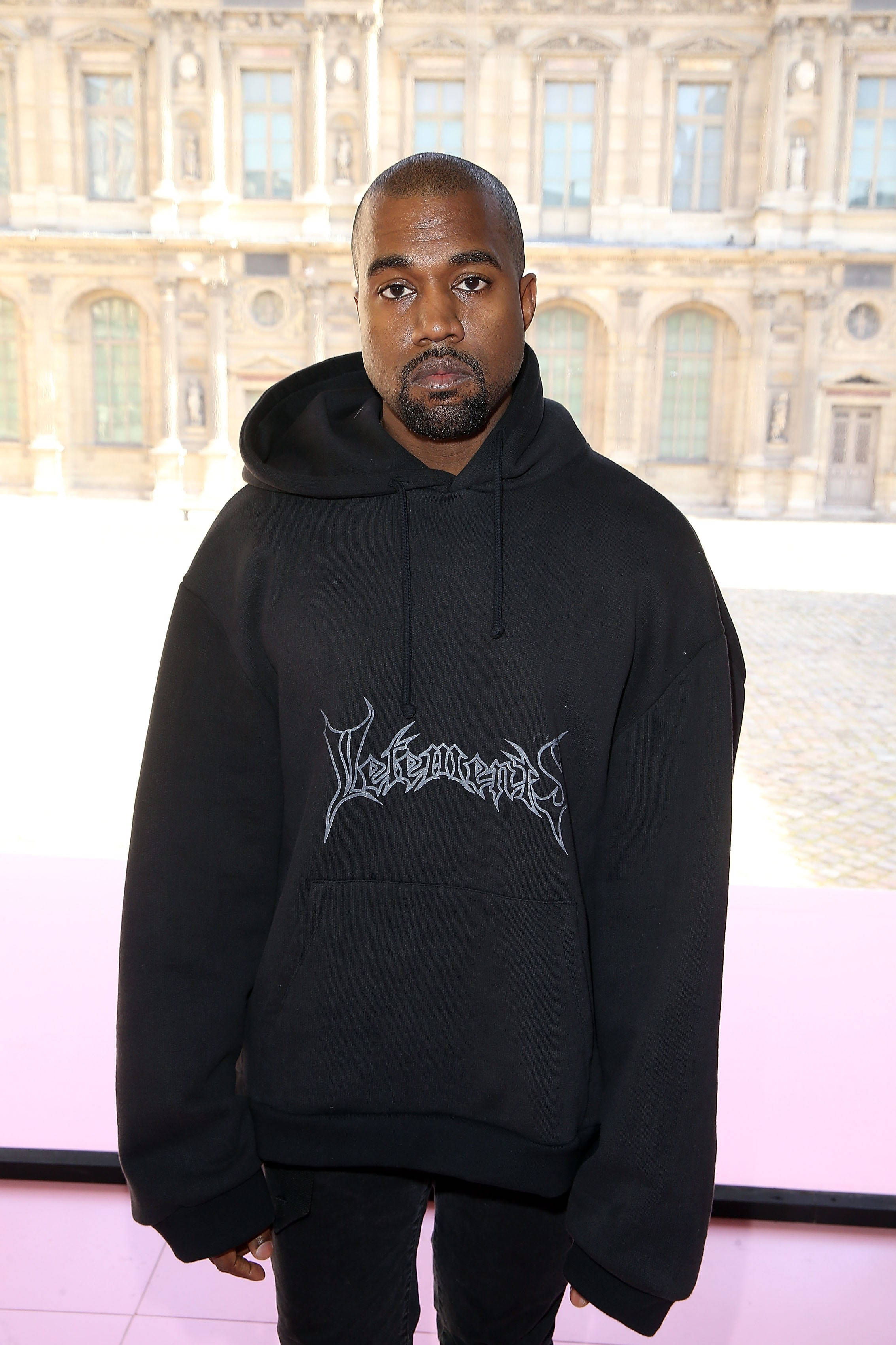 Kanye 身穿 Vetements 超大號連帽衫 壁紙 — Kanye West 身穿印有 'Vetements' 標誌的黑色連帽衫，站在宏偉的石砌建築外牆前。