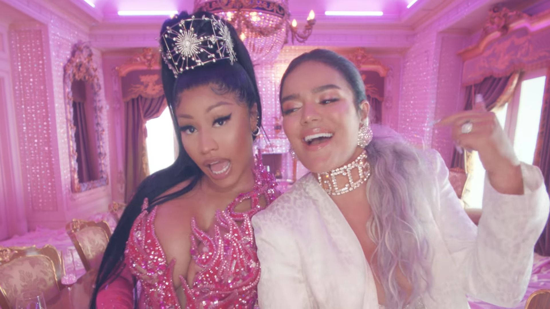 Karol G 與 Nicki Minaj 在 Tusa 中 壁紙 — 兩位魅力女性在豪華粉紅色主題房間中，在紫色燈光下以大膽表情和閃亮珠寶擺姿勢。