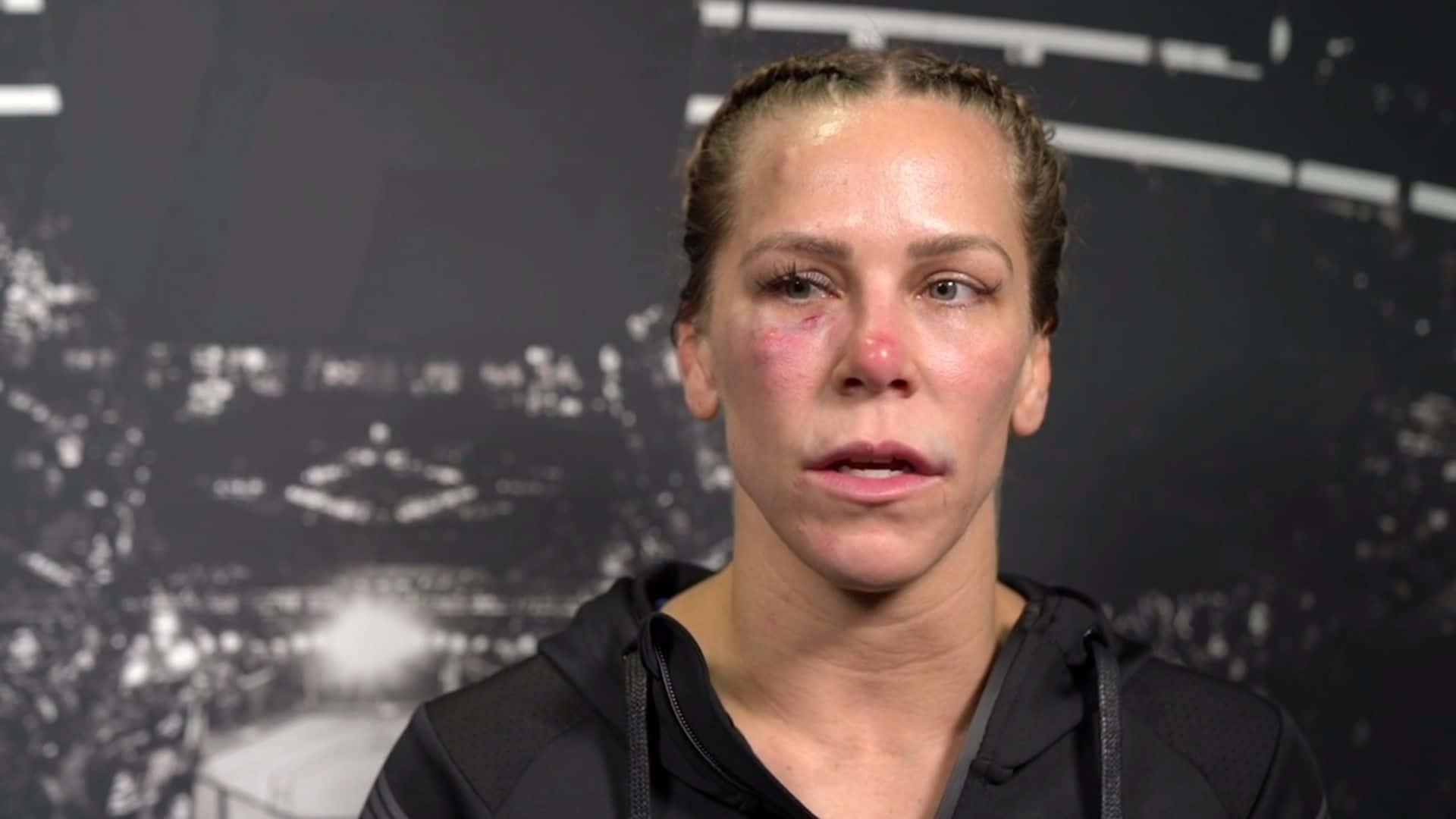 Katlyn Chookagian被打得遍體鱗傷 壁紙 — 一位女戰士身上有明顯瘀傷，身穿黑色連帽衫，站在模糊的黑白競技場背景前。