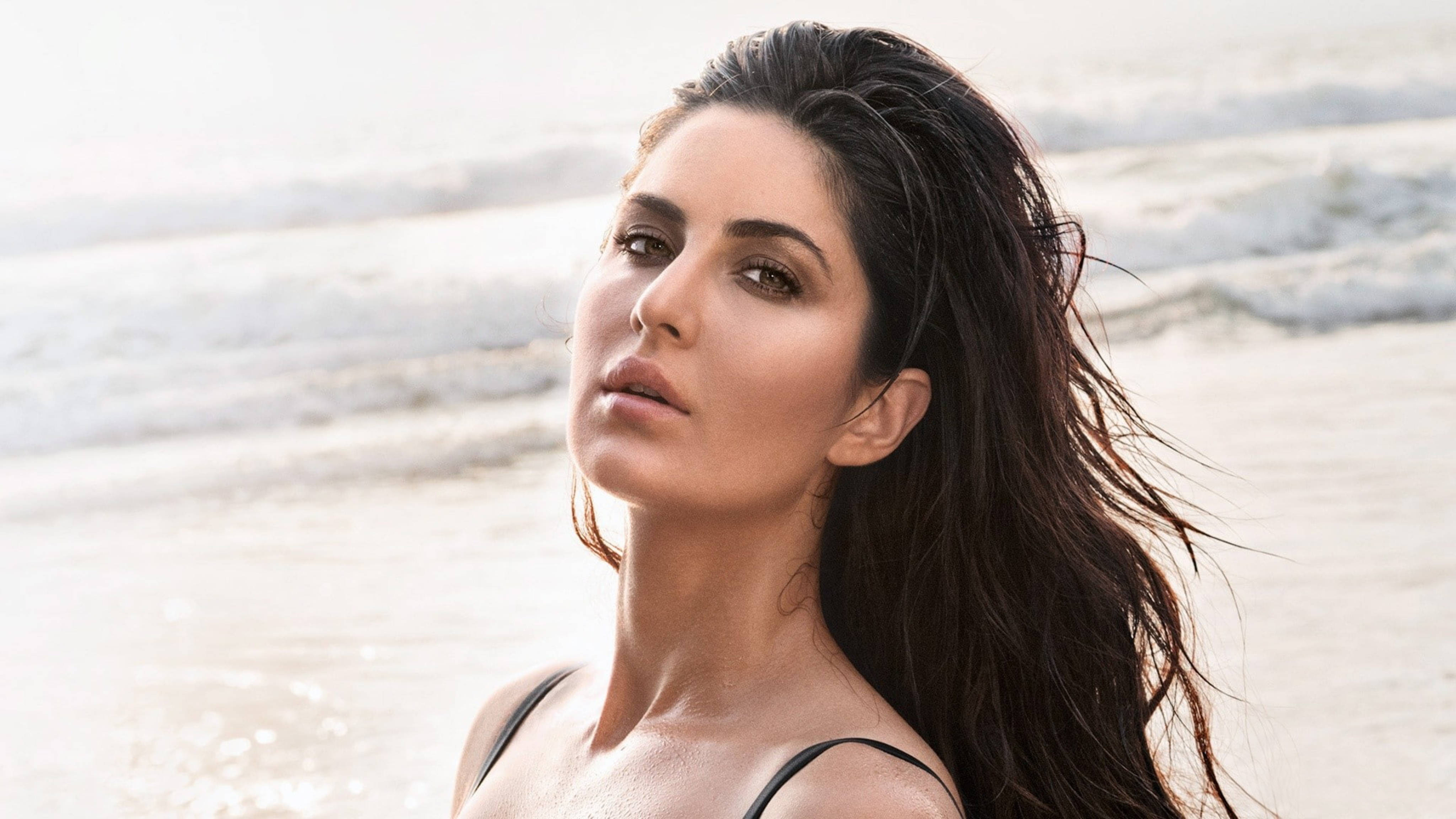 Katrina Kaif GQ海灘拍攝 壁紙 — 一位擁有濕黑頭髮的女性站在海灘上，身後的海浪在柔和日光中拍打。