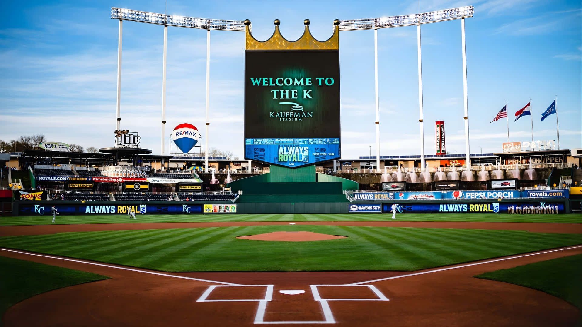  壁紙 — 晴朗藍天下，Kauffman Stadium 棒球場的廣角鏡頭，標誌性的皇冠計分板顯示著「Welcome to the K」。