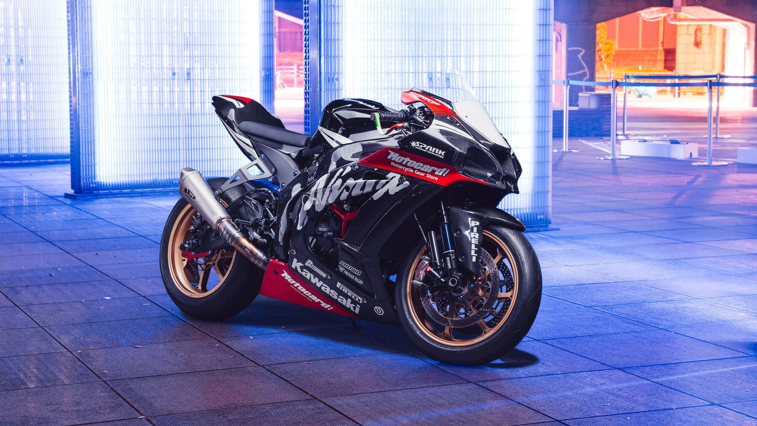震撼的Kawasaki Ninja ZX10R機車背景 壁紙 — 一架時尚的黑紅配色 Kawasaki Ninja 跑車在夜晚的現代城市廣場上，在鮮豔的藍色霓虹燈下閃閃發光。