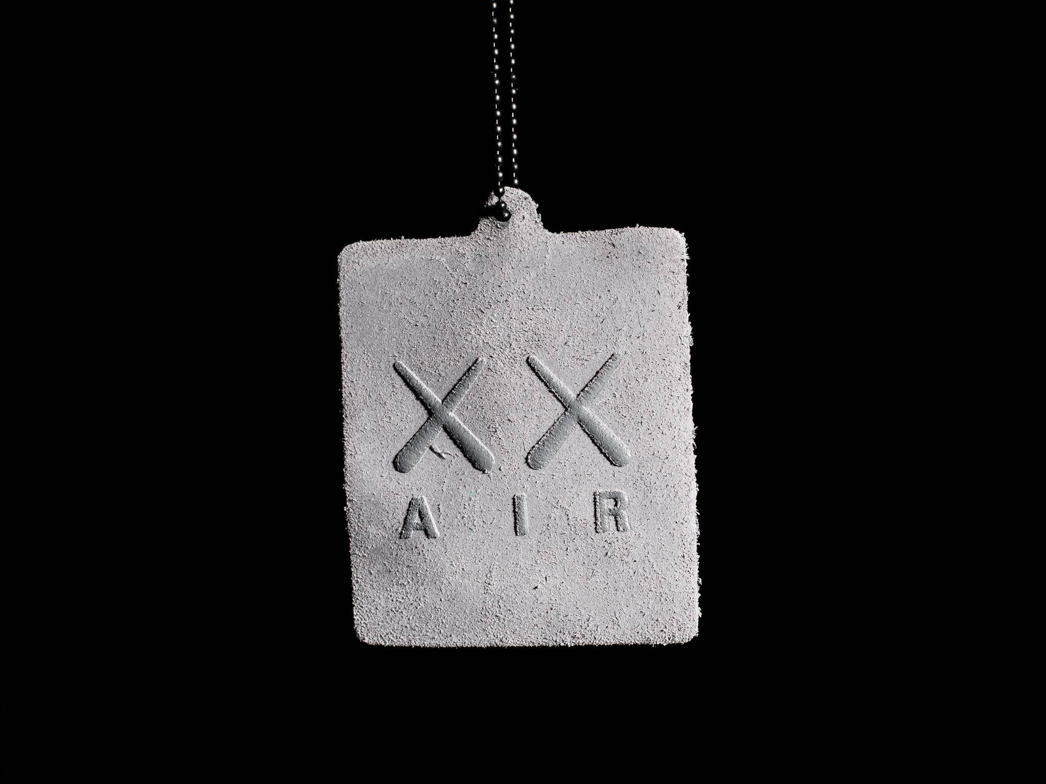 KAWS Air Jordan標籤 壁紙 — 一個極簡的水泥標籤，帶有浮雕X和AIR，掛在純黑背景上。