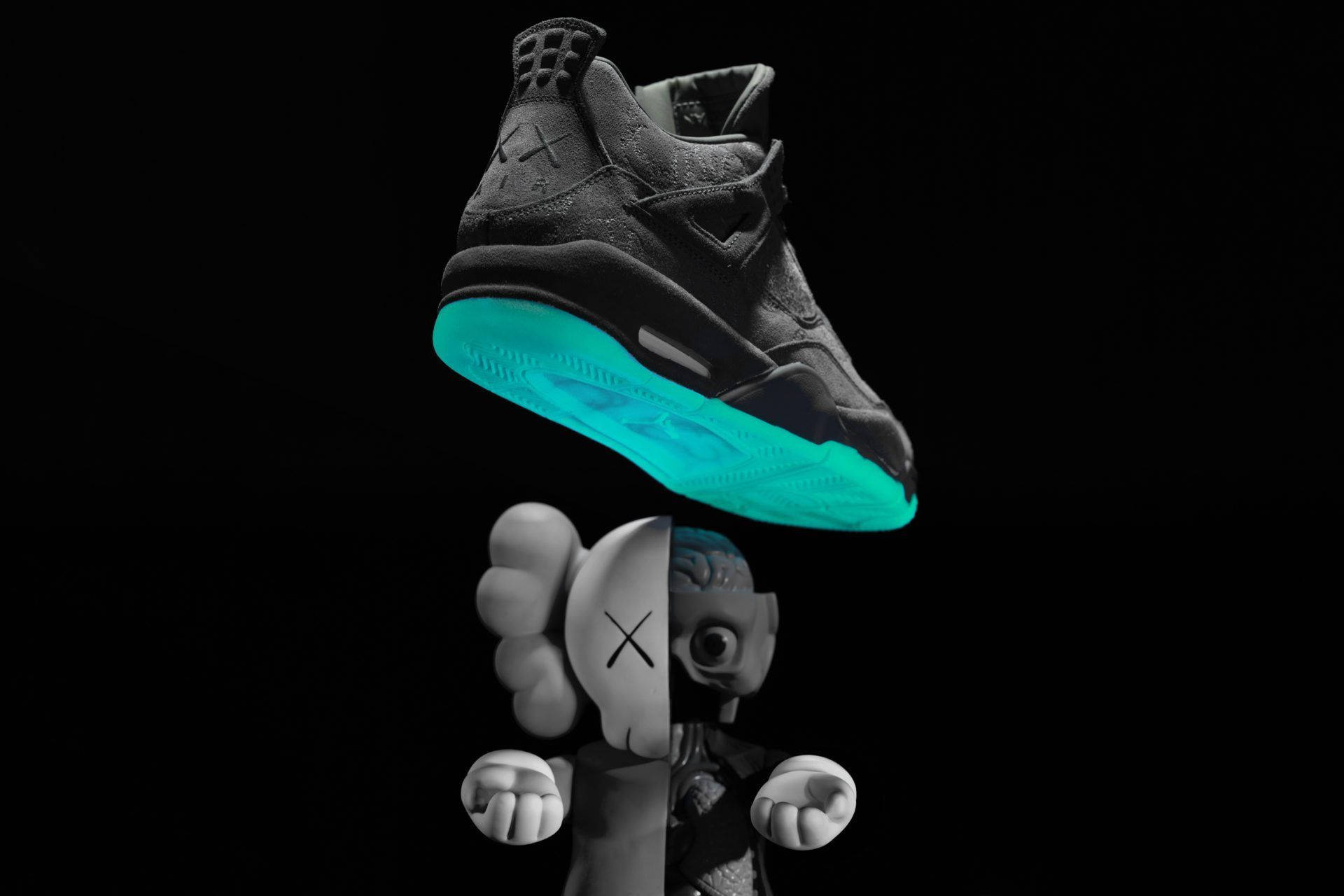 KAWS Air Jordan球鞋 壁紙 — 一對黑色運動鞋帶有發光青色鞋底，懸浮在黑色背景上的分裂面孔KAWS公仔上方。