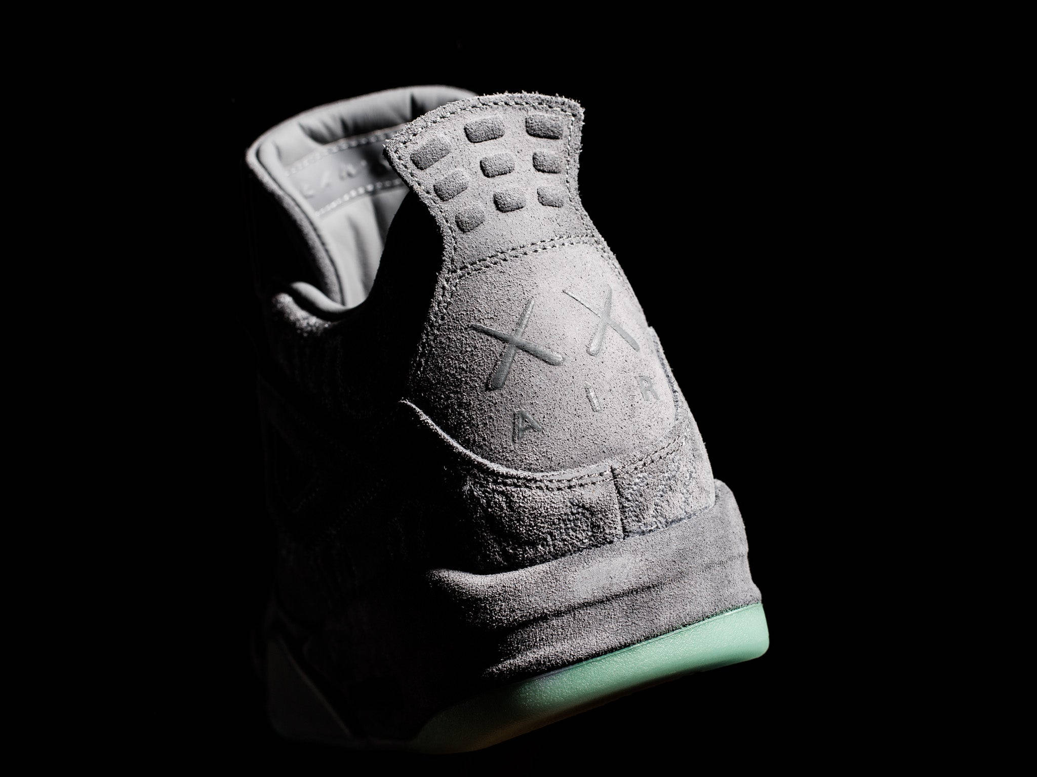 KAWS Air Jordan鞋跟標誌 壁紙 — 一雙時尚的灰色麂皮運動鞋，搭配薄荷綠色鞋底，在純黑色背景上閃耀。