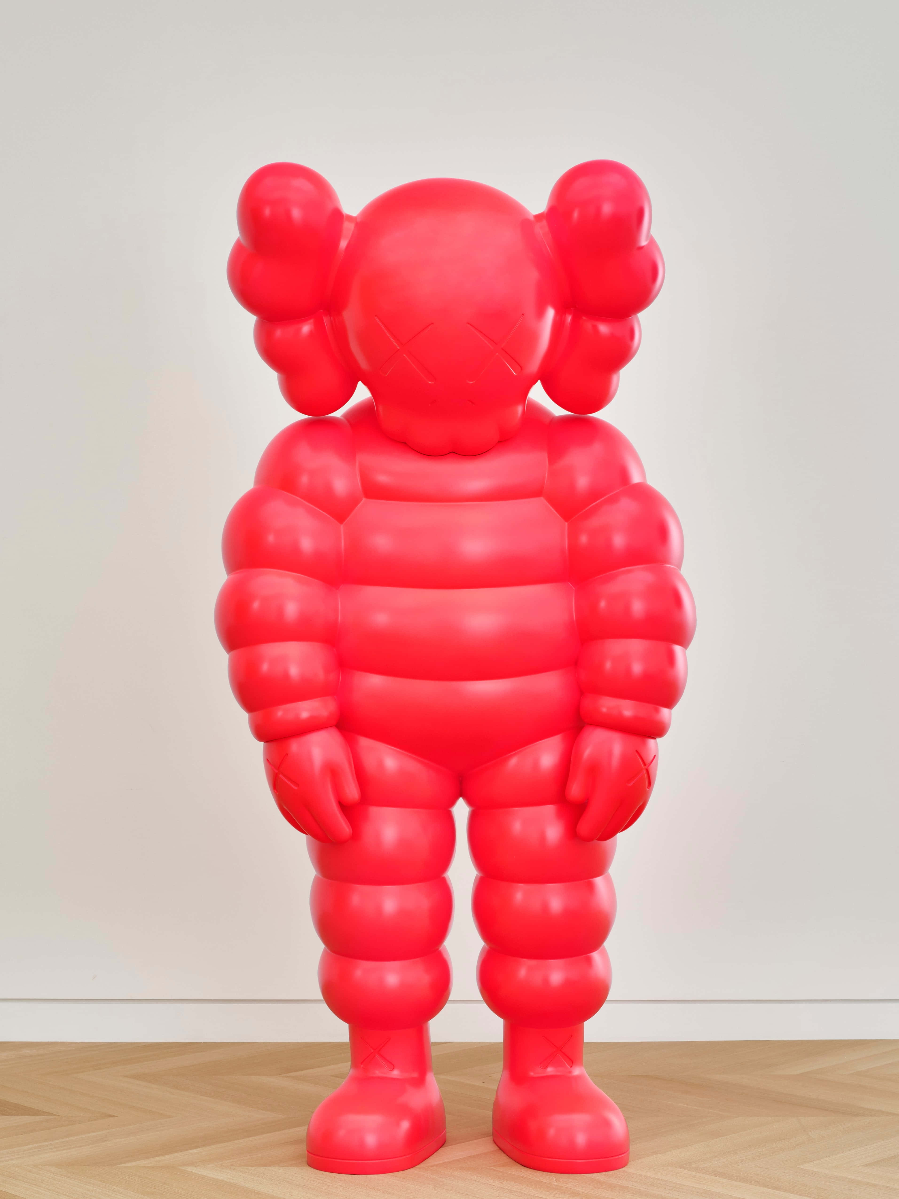 KAWS 的經典藝術作品 壁紙 — 一個光澤亮麗的紅色KAWS Companion雕塑高高地立在木地板上，背景是純白牆壁。