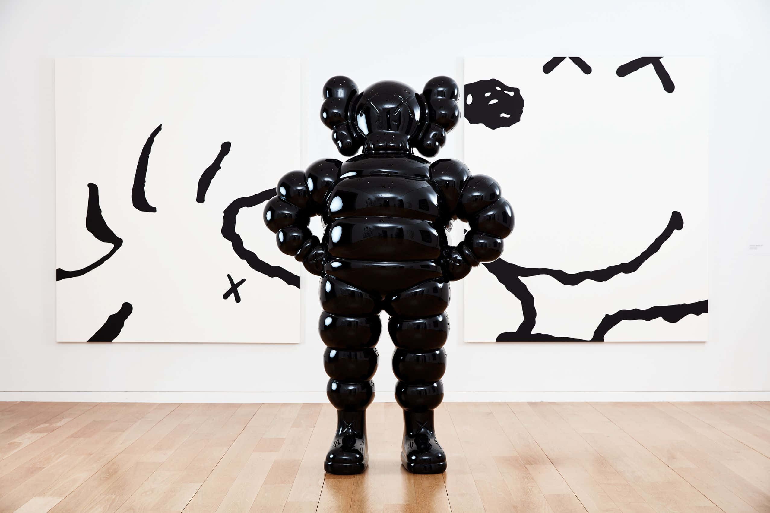 KAWS — 經典都市藝術家 壁紙 — 一個亮黑色的KAWS Companion雕像雙手叉腰，面向極簡主義畫廊中的抽象黑色畫作。