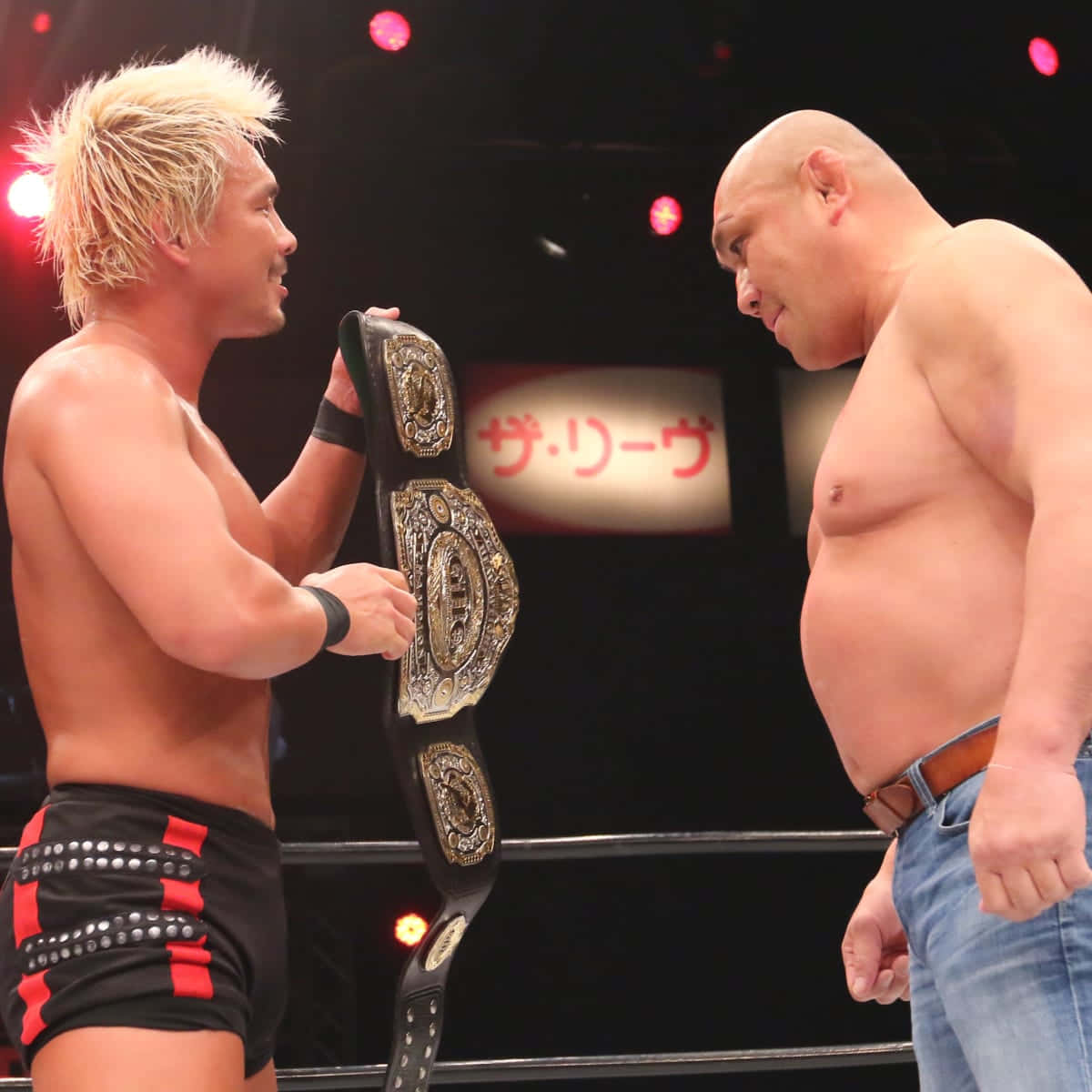 Kazuyuki Fujita與Katsuhiko Nakajima於Sendai Bumper Crop 2022對戰 壁紙 — 兩名肌肉發達的摔角手在擂台上對峙，其中一人手持冠軍腰帶，在明亮的場館燈光下。
