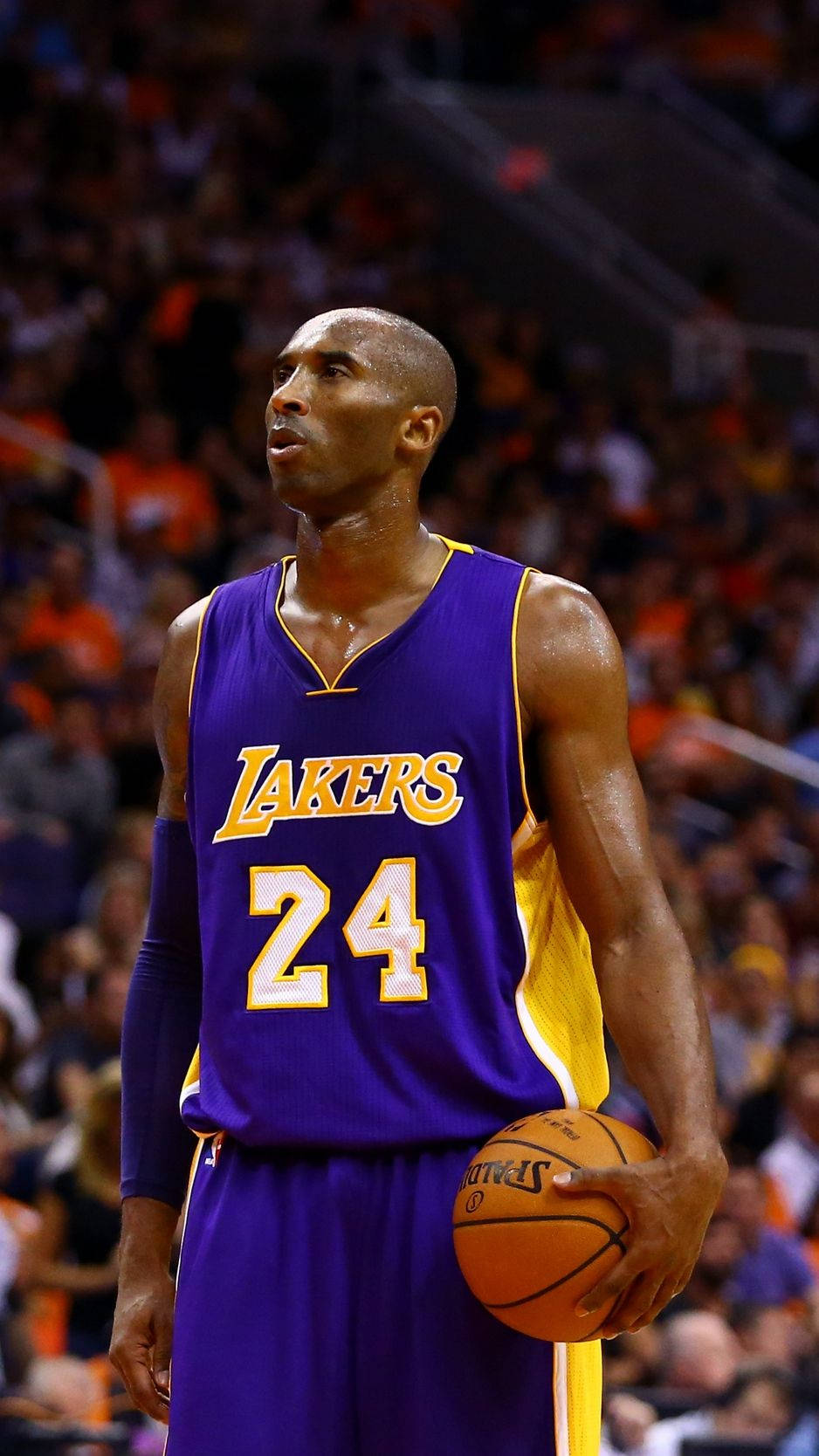 NBA冠軍科比·布萊恩特 iPhone 壁紙 — 高比·拜仁身穿湖人隊24號球衣，在場館燈光下專注地持球比賽。