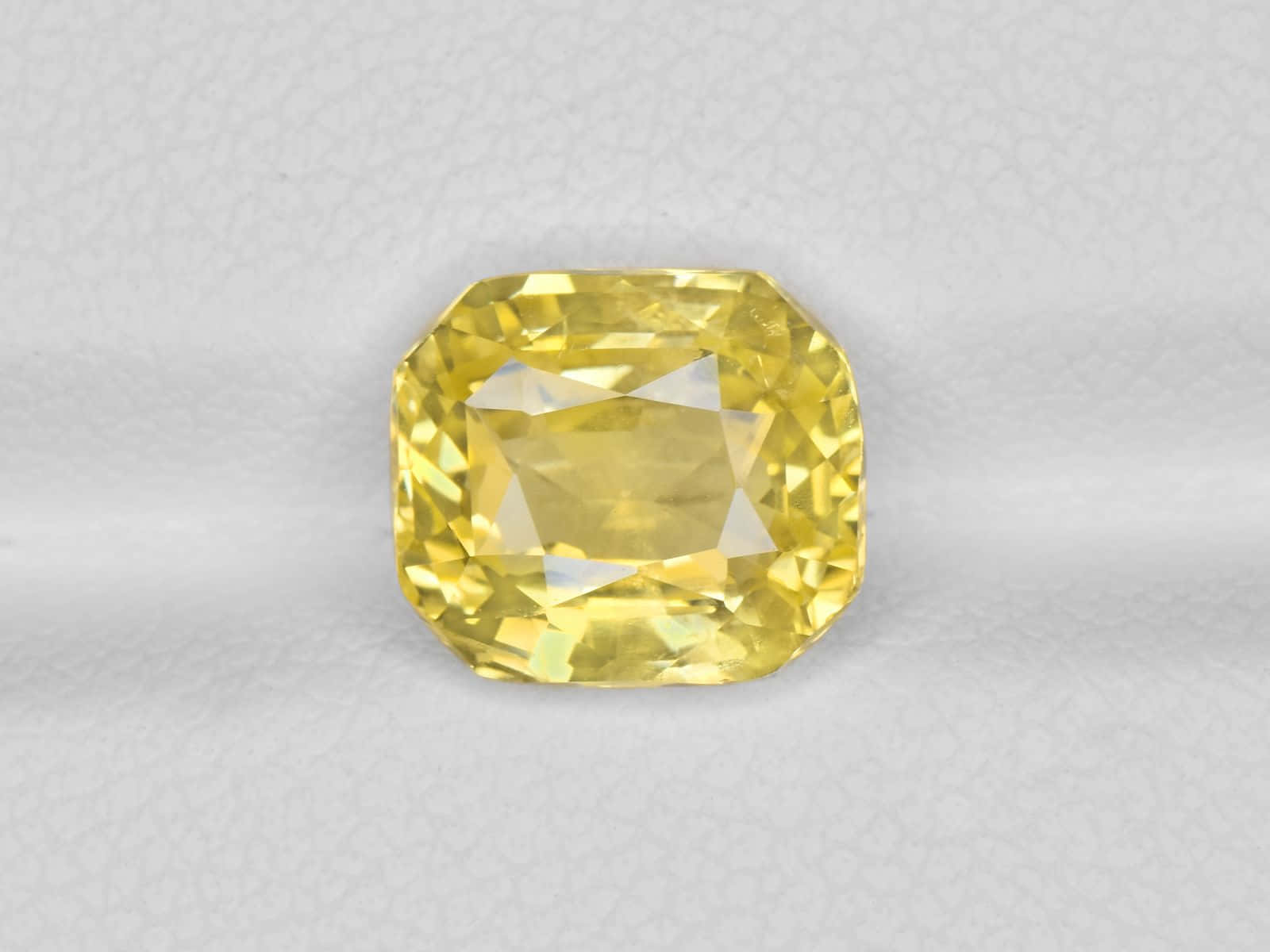Yellow Sapphire 桌布 壁紙 — 一顆明亮的黃色枕形切割寶石，在柔軟的紋理灰色背景上閃耀著精確的刻面。