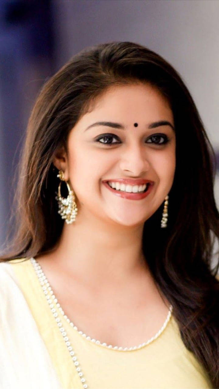 泰米尔女星 Keerthy Suresh 高畫質影像 壁紙 — 一位長黑髮的耀眼女性，身穿黃色上衣和珍珠首飾，溫暖地微笑。