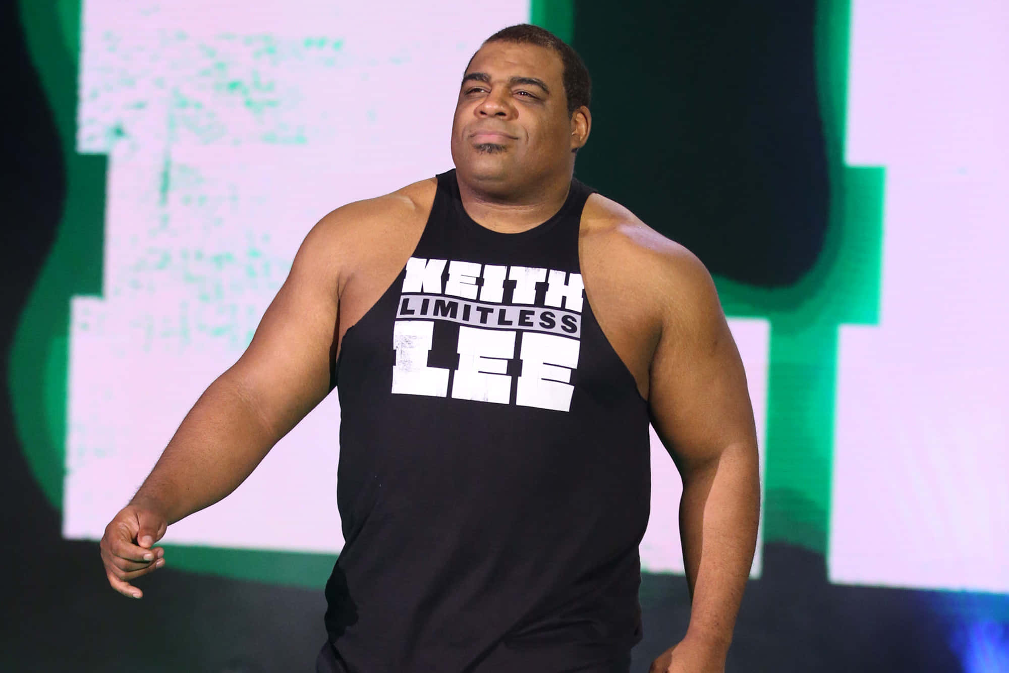 Keith Lee — The Limitless One身穿黑色單衣 壁紙 — 摔角手 Keith Lee 身穿印有白色文字的黑色背心，在明亮燈光下自信地站在舞台上。