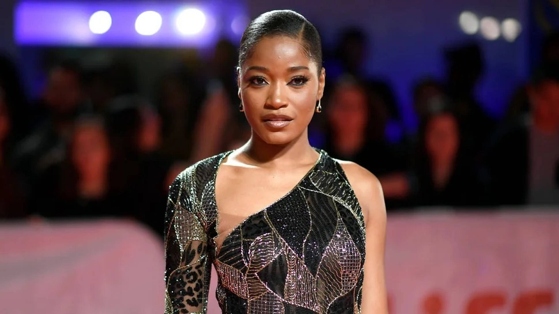 Keke Palmer 2019 年多倫多國際影展 壁紙 — 一位優雅自信的女性身穿閃爍的黑色和金色單肩禮服，在明亮的活動燈光下自信地站在紅地毯上。