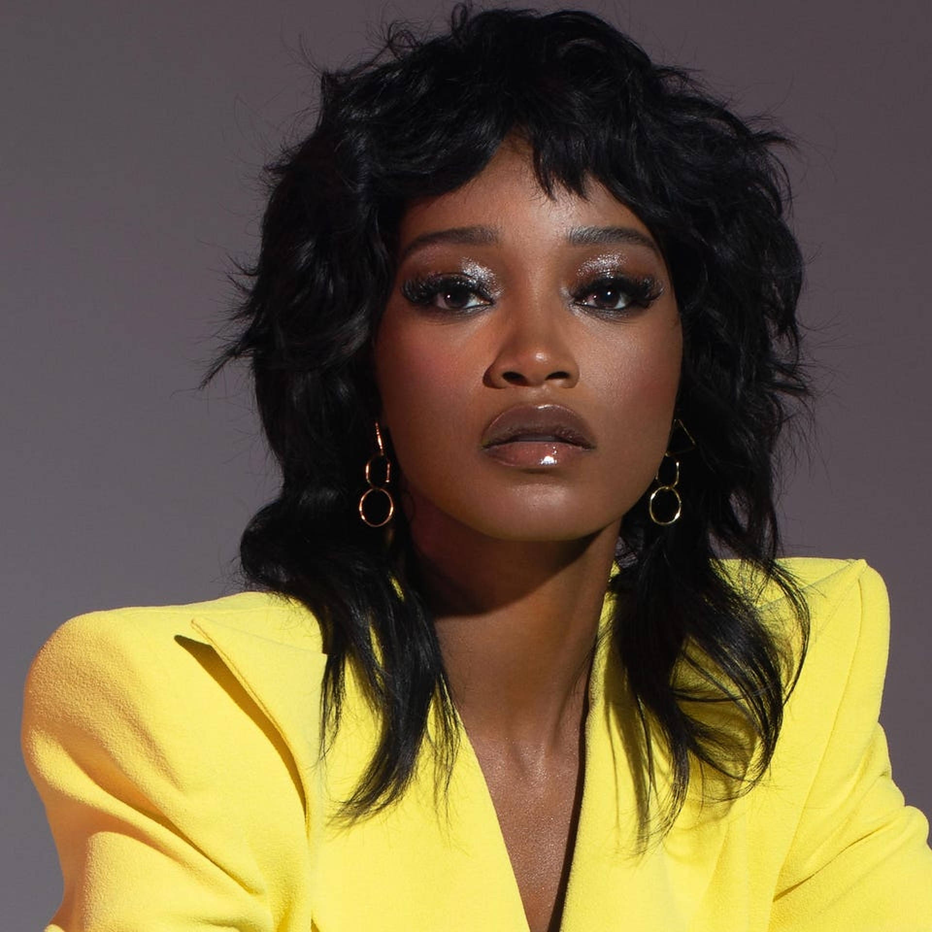 Keke Palmer 肖像照 壁紙 — 一位擁有豐盈黑髮和閃亮眼睛的女性，穿著大膽的黃色西裝外套，引人注目的肖像。