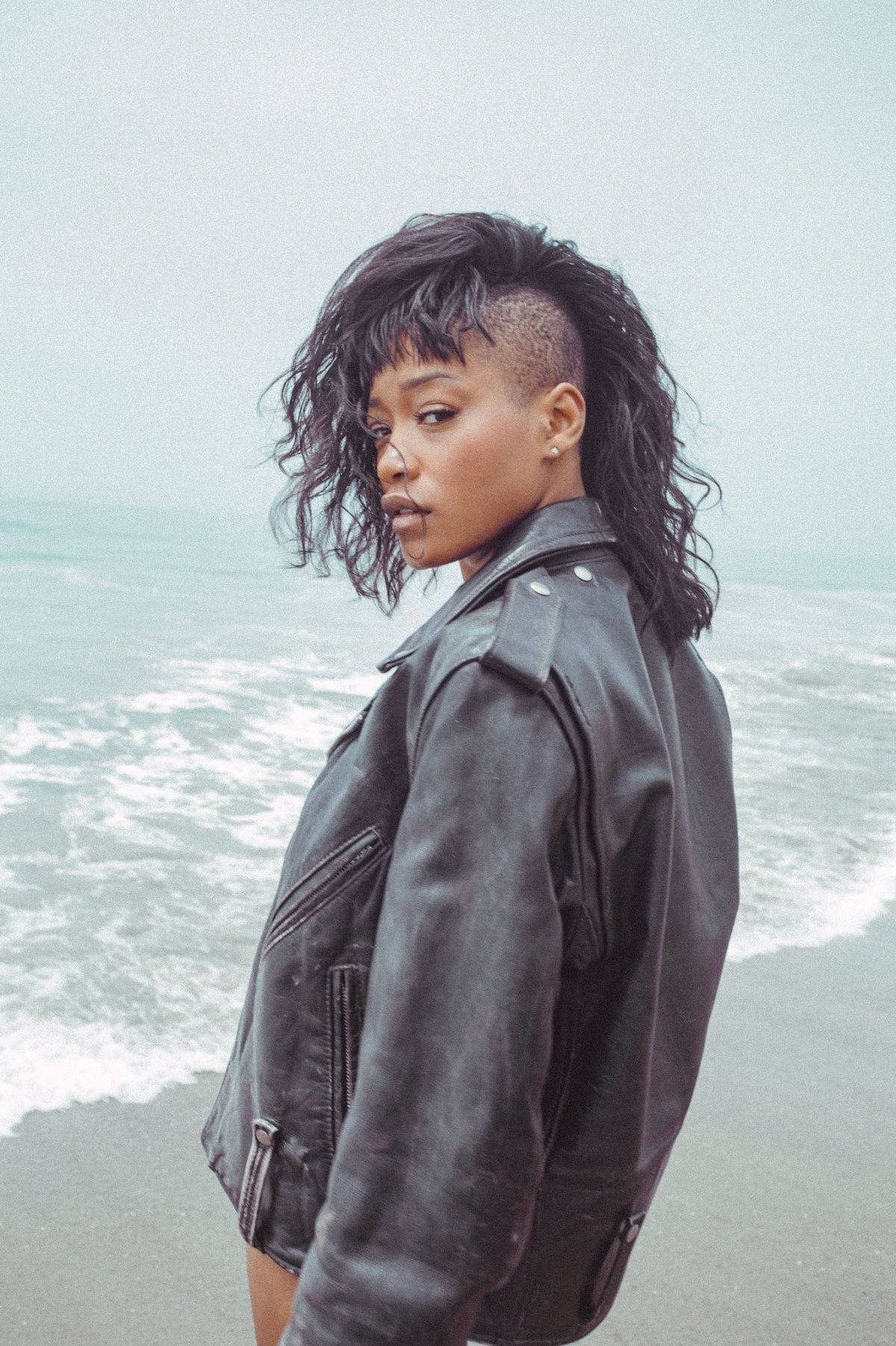 Keke Palmer 海灘寫真 壁紙 — 一位擁有大膽髮型的女性自信地站在霧濛濛的海灘上，身後海浪拍打。
