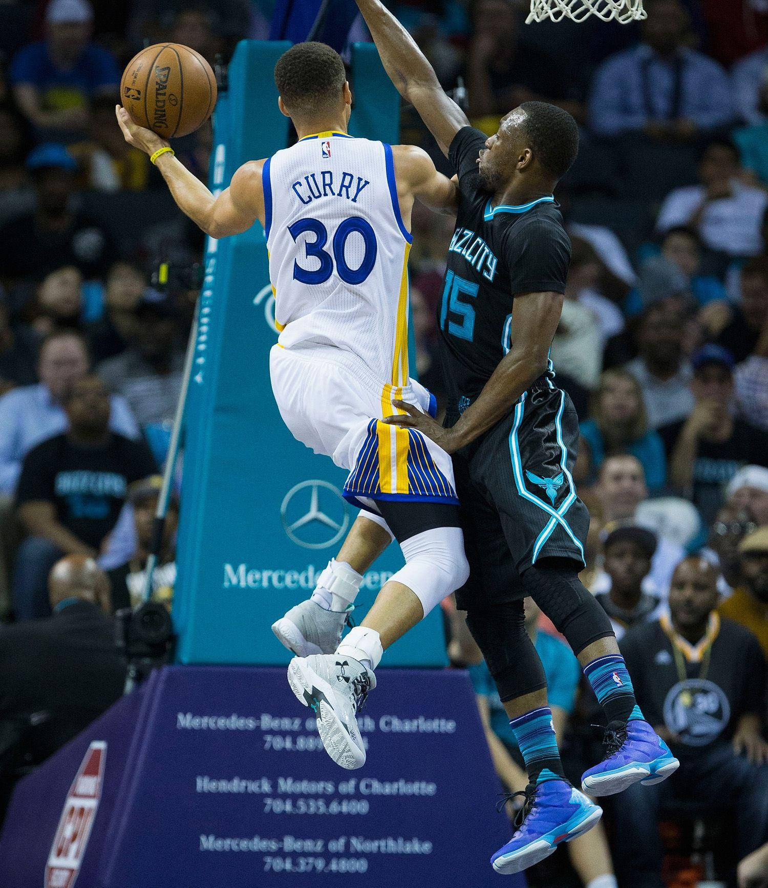Kemba Walker 對決史蒂芬·柯瑞壁紙 壁紙 — 一名身穿白色球衣的籃球運動員在激烈的比賽中跳向籃框，同時被一名身穿黑色球衣的對手防守。