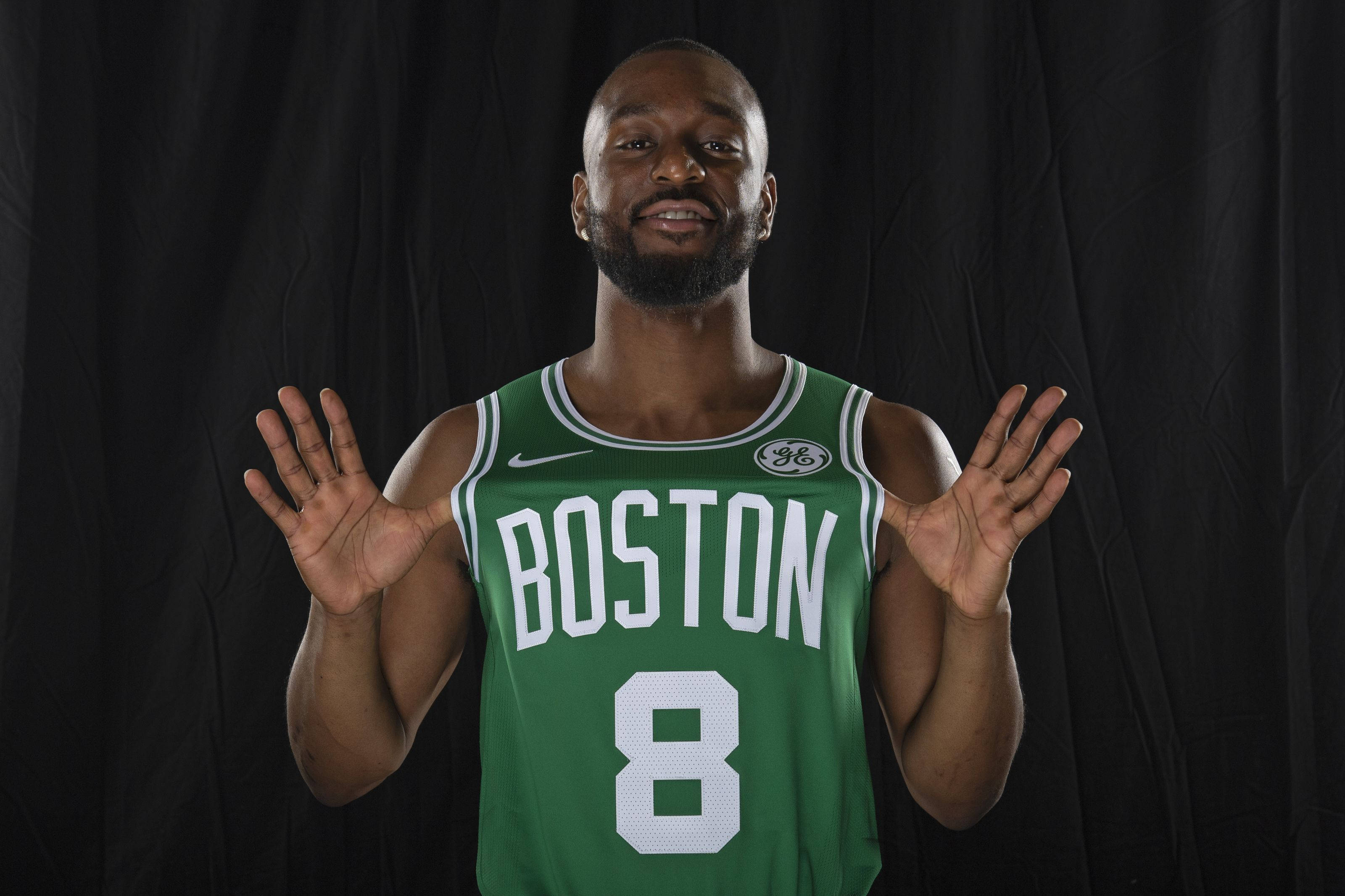 Kemba Walker 波士頓塞爾提克隊個人照壁紙 壁紙 — 一名身穿綠色波士頓球衣8號的籃球運動員在黑色背景前張開雙手微笑。